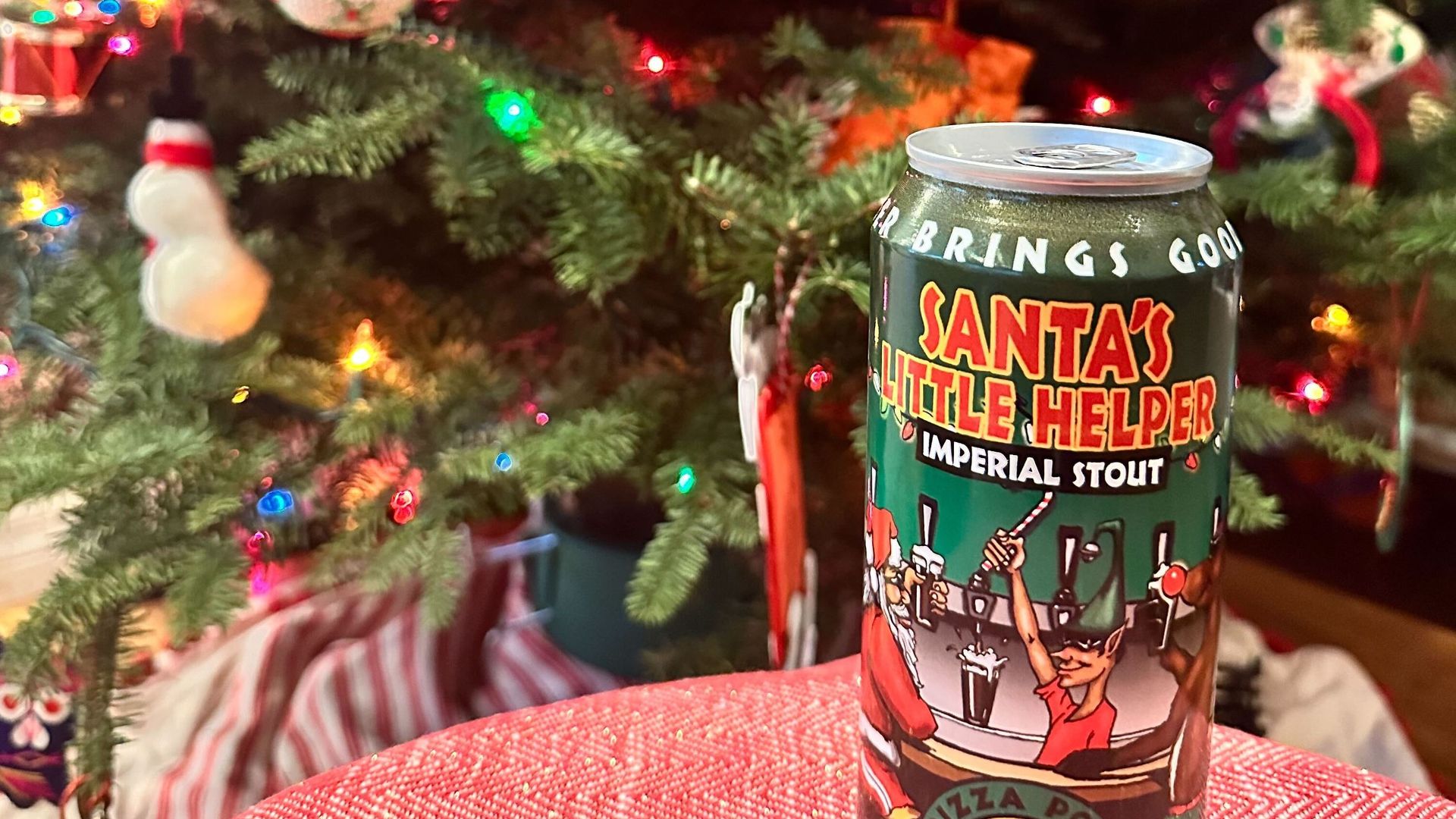 A holiday-themed beer can sits in front of a Christmas tree.