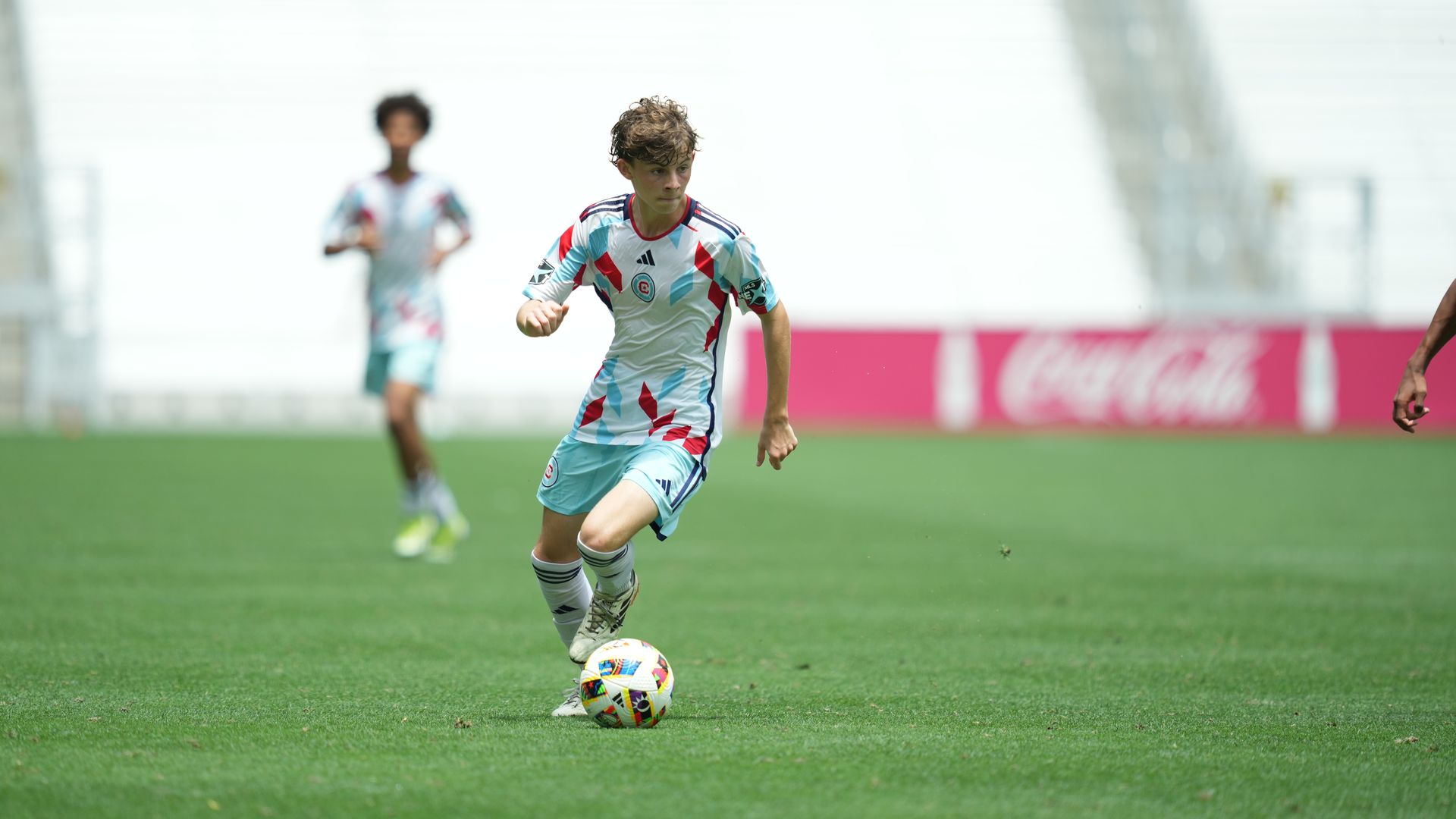Photo of a soccer playing running down a field while kicking a soccer ball 
