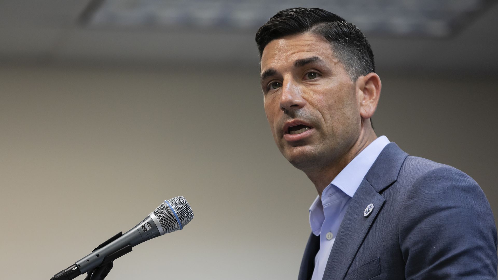 Chad Wolf in a suit stands in front of a microphone 