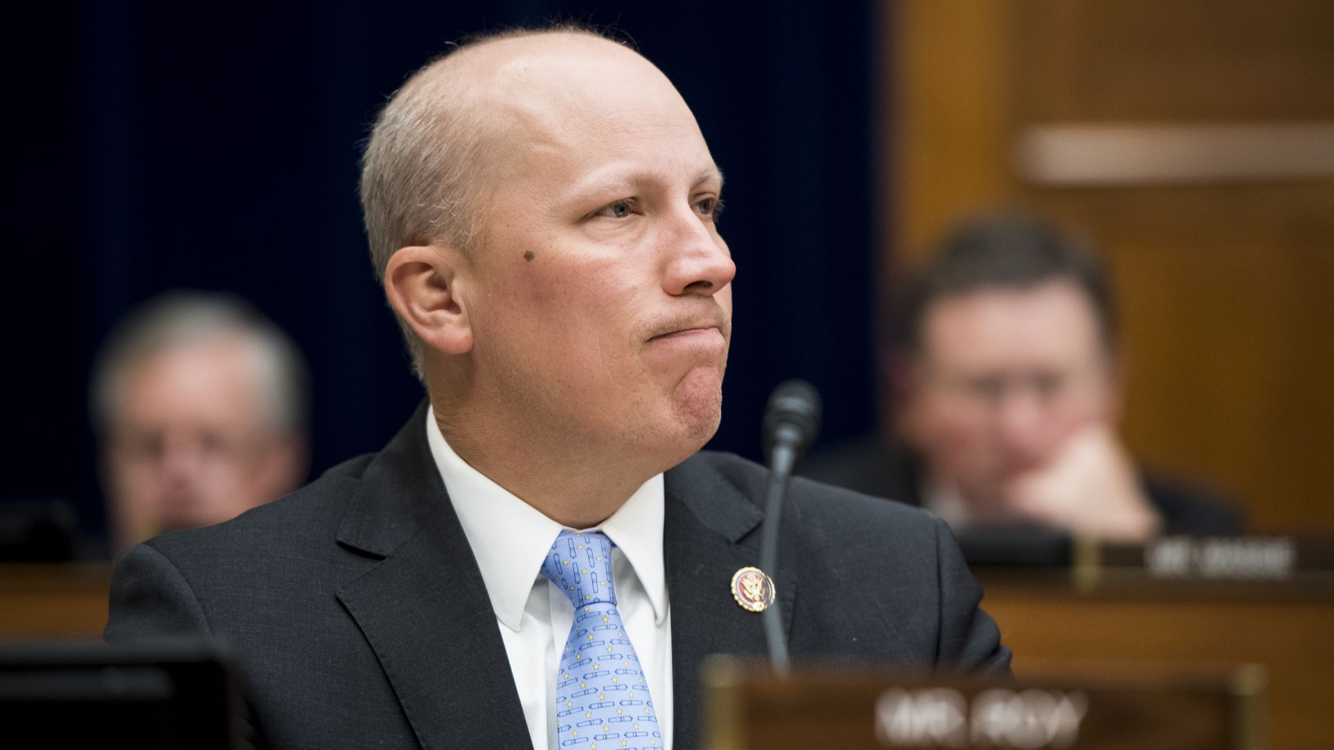 In this image, Chip Roy sits in a suit and listens in front of a microphone.