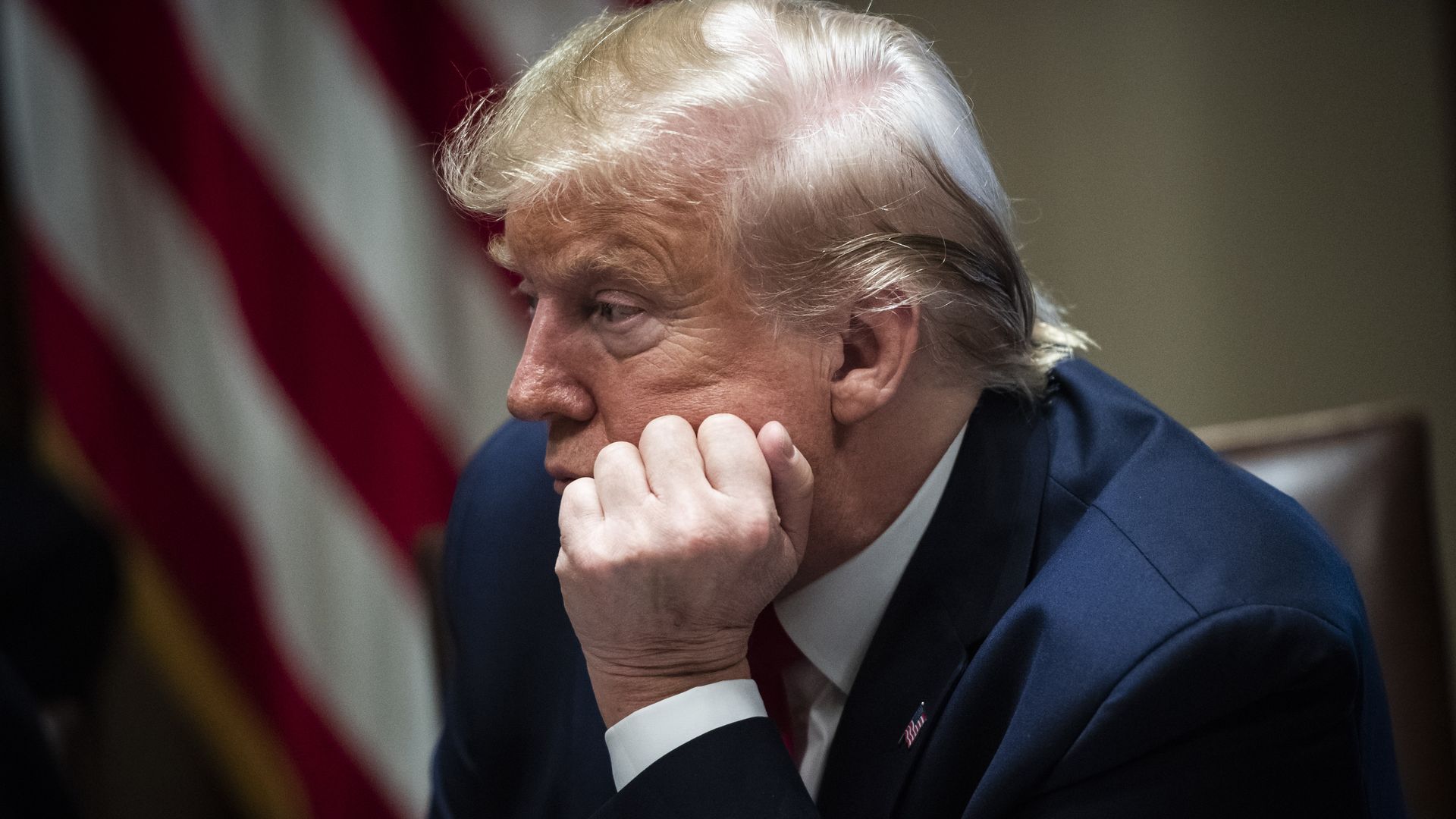 In this image, President Trump sits in a suit and listens