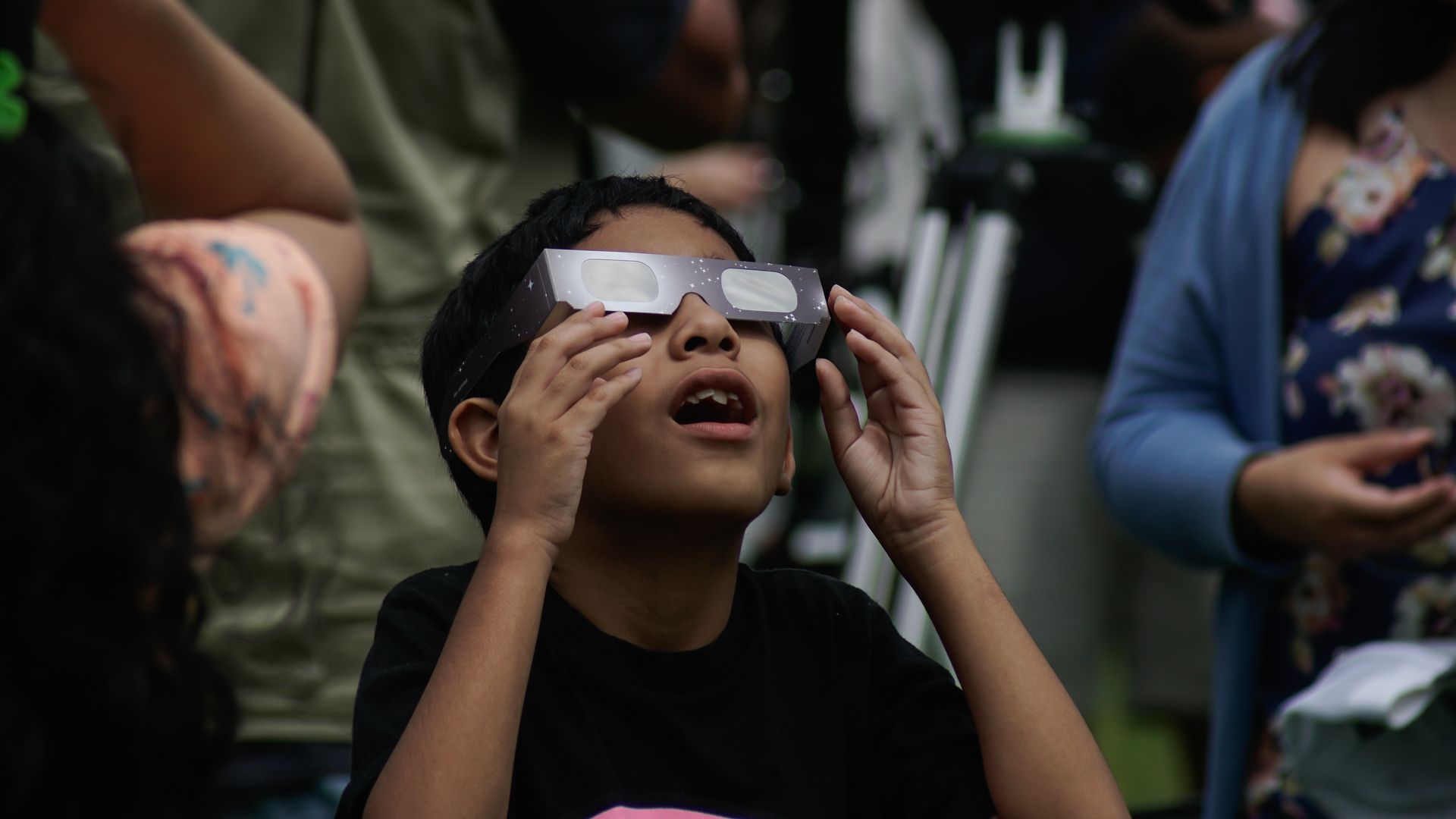 A child wearing solar eclipse glasses looks up at the sky with his mouth open in awe.