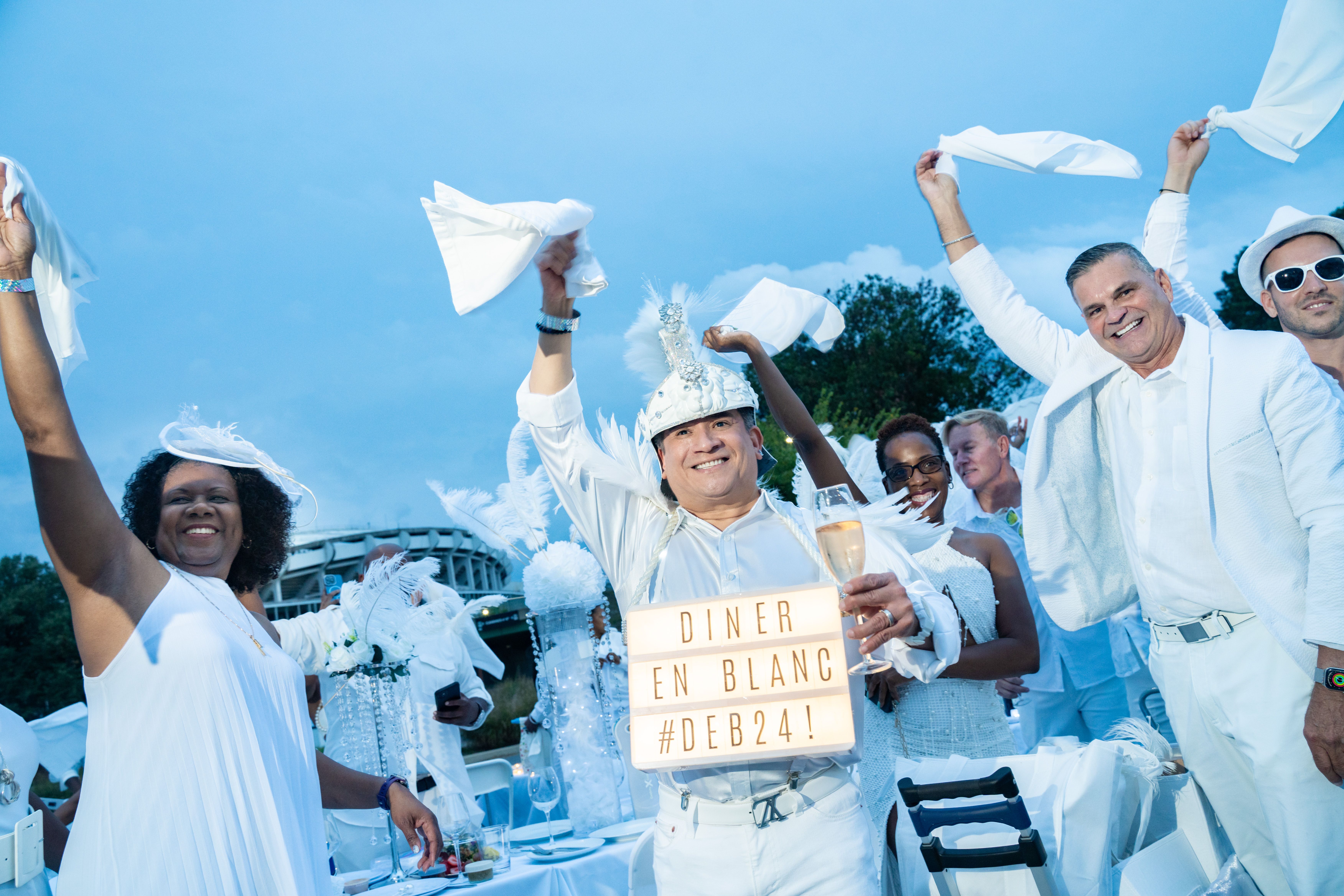 Guests dressed in all-white waving napkins with RFK Stadium in the background 