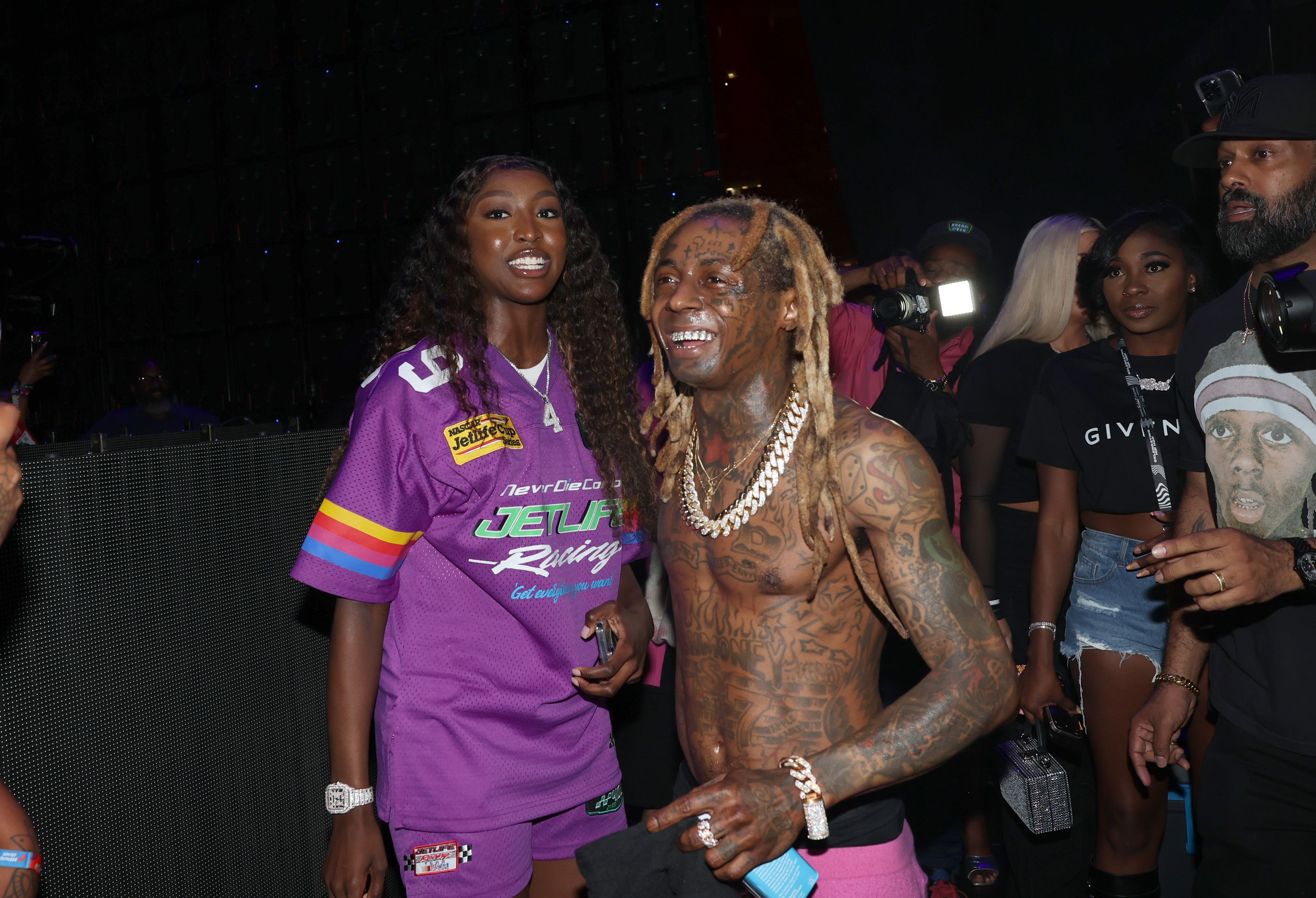 Flau'jae Johnson smiles at the camera as Lil Wayne walks past.