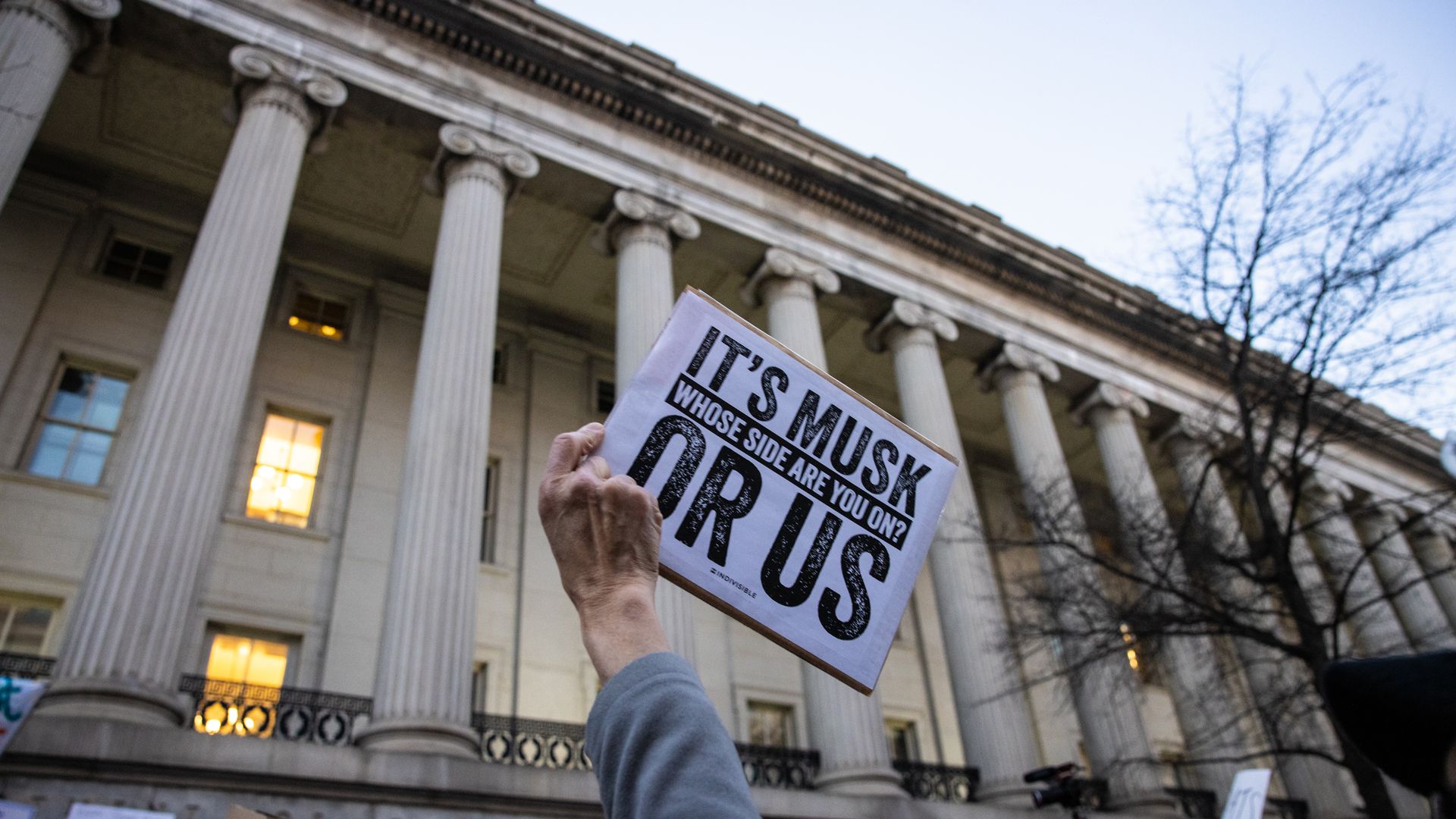  demonstrator holds up a sign during a rally in front of the U.S. Treasury Department that reads "It's Musk or Us" and "Whose side are you on?"