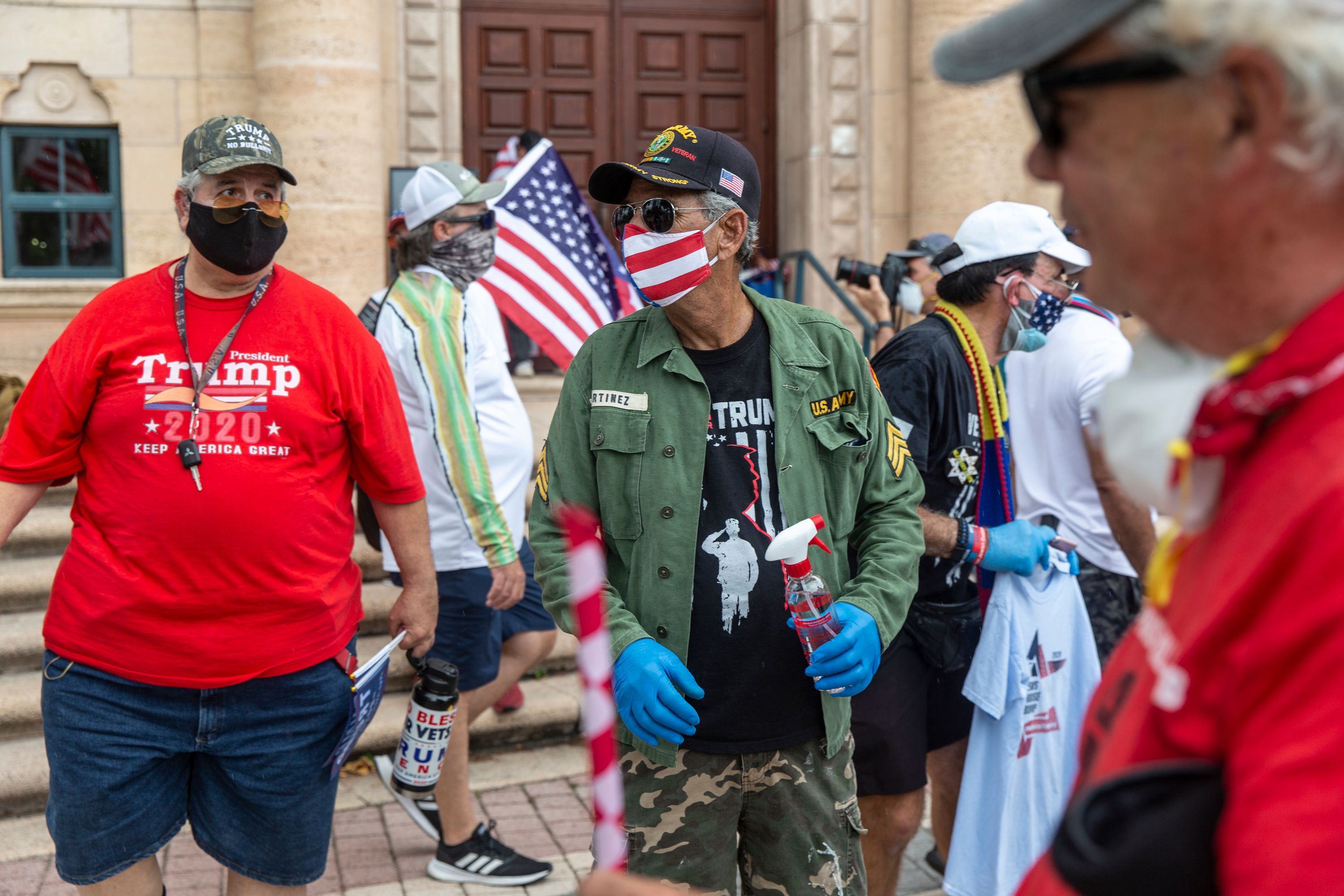 In this image, men wear face masks and sunglasses and stand outside.