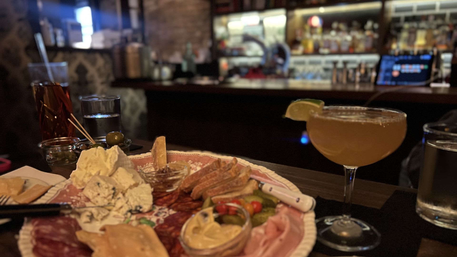 An image of a plate of cheese with a cocktail glass in the background.