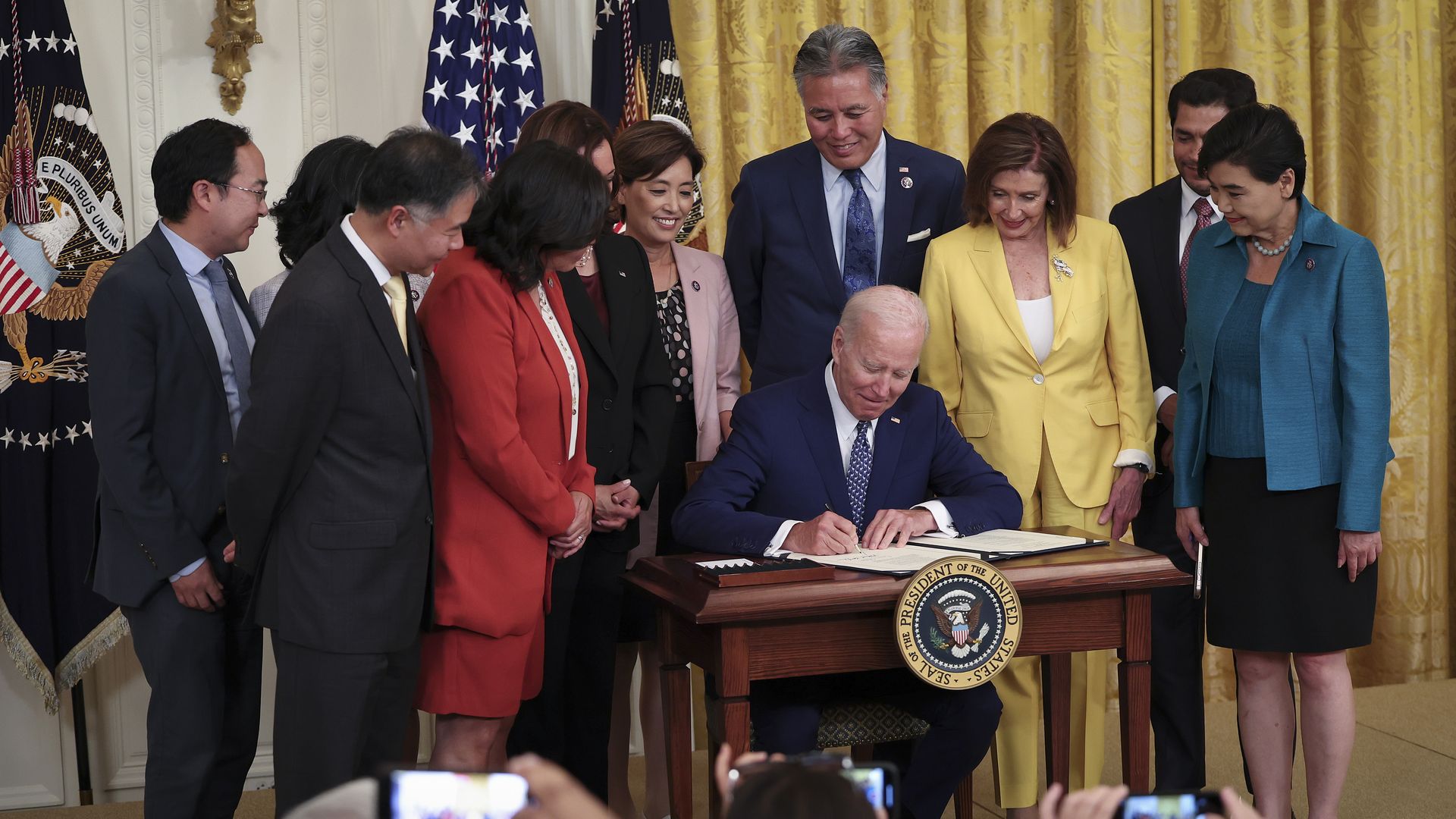 Photo of Joe Biden signing a bill at a table while Congress members stand around him watching