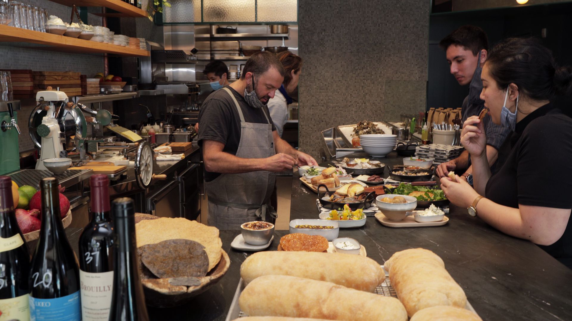 Photo of a chef plating dishes on a counter while two employees watch