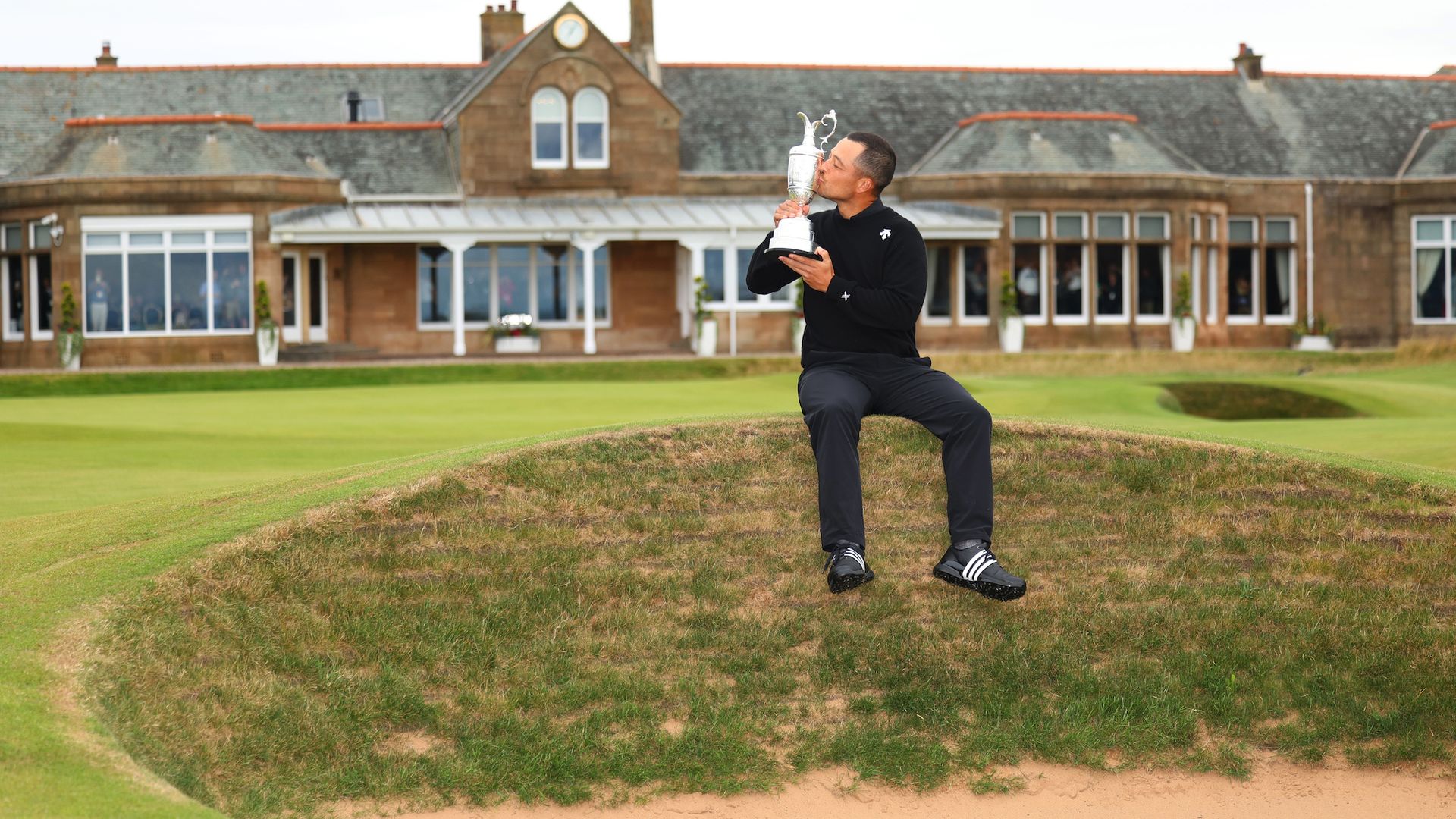 Xander Schauffele kisses a trophy on the 18th hole at a golf course.