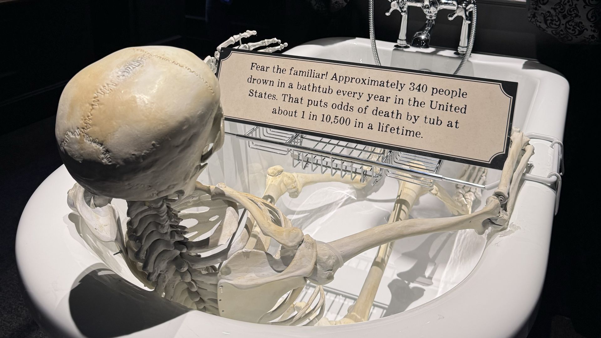 A fake skeleton sits in a bathtub in front of a sign that says "Fear the familiar! Approximatel 340 people drown in a bathtub every year in the United States. That puts odds of death by tub at about 1 in 10,500 in a lifetime."
