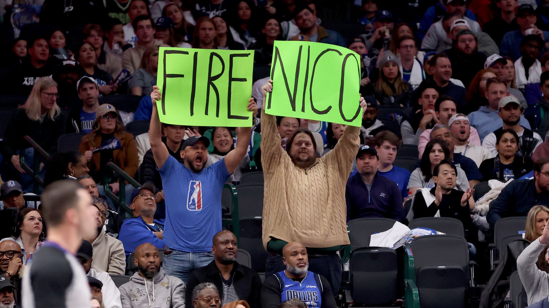 Fans hold up neon green signs that say Fire Nico at a Dallas Mavericks game