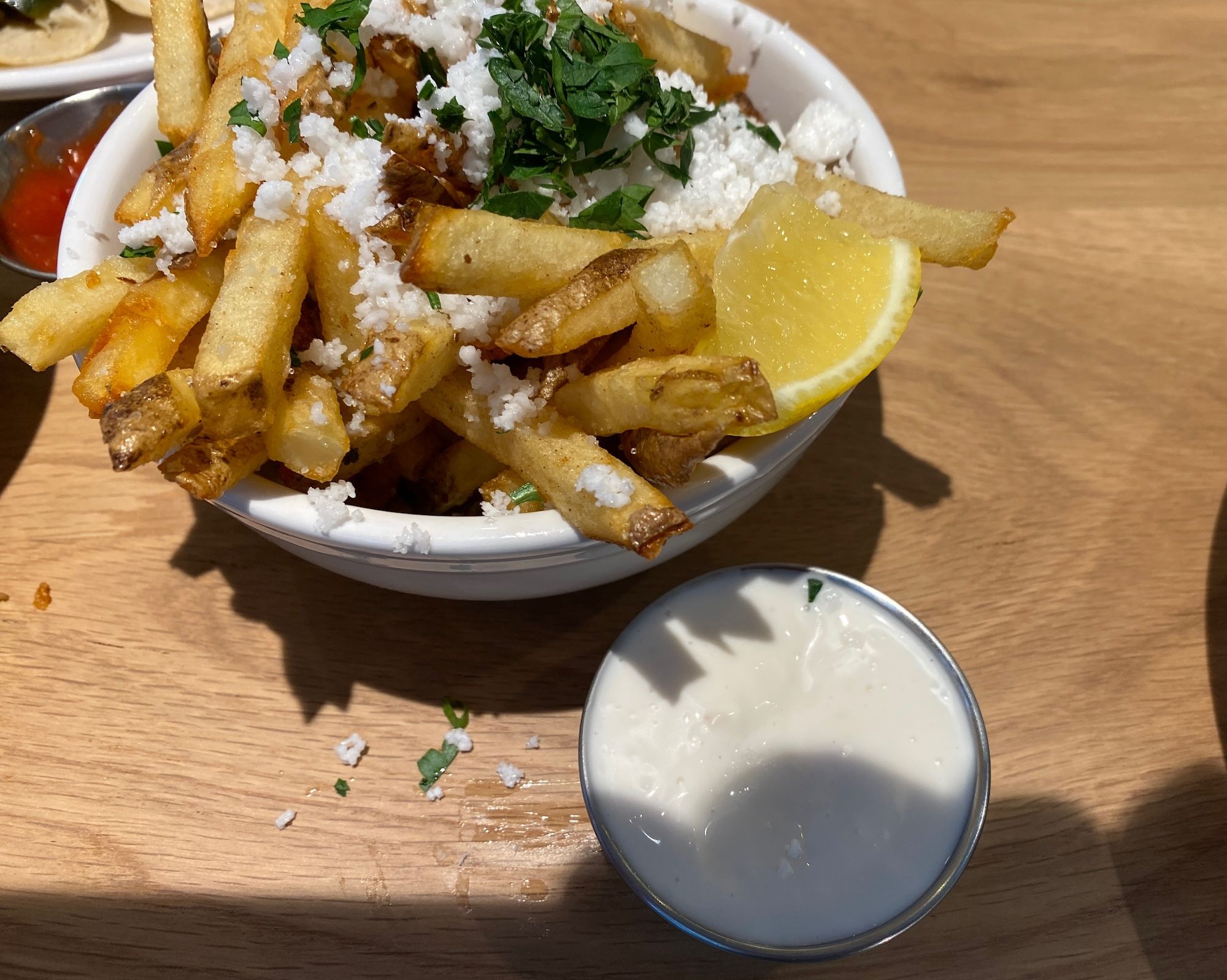 French fries with white cheese, lemon and parsley in white bowl.