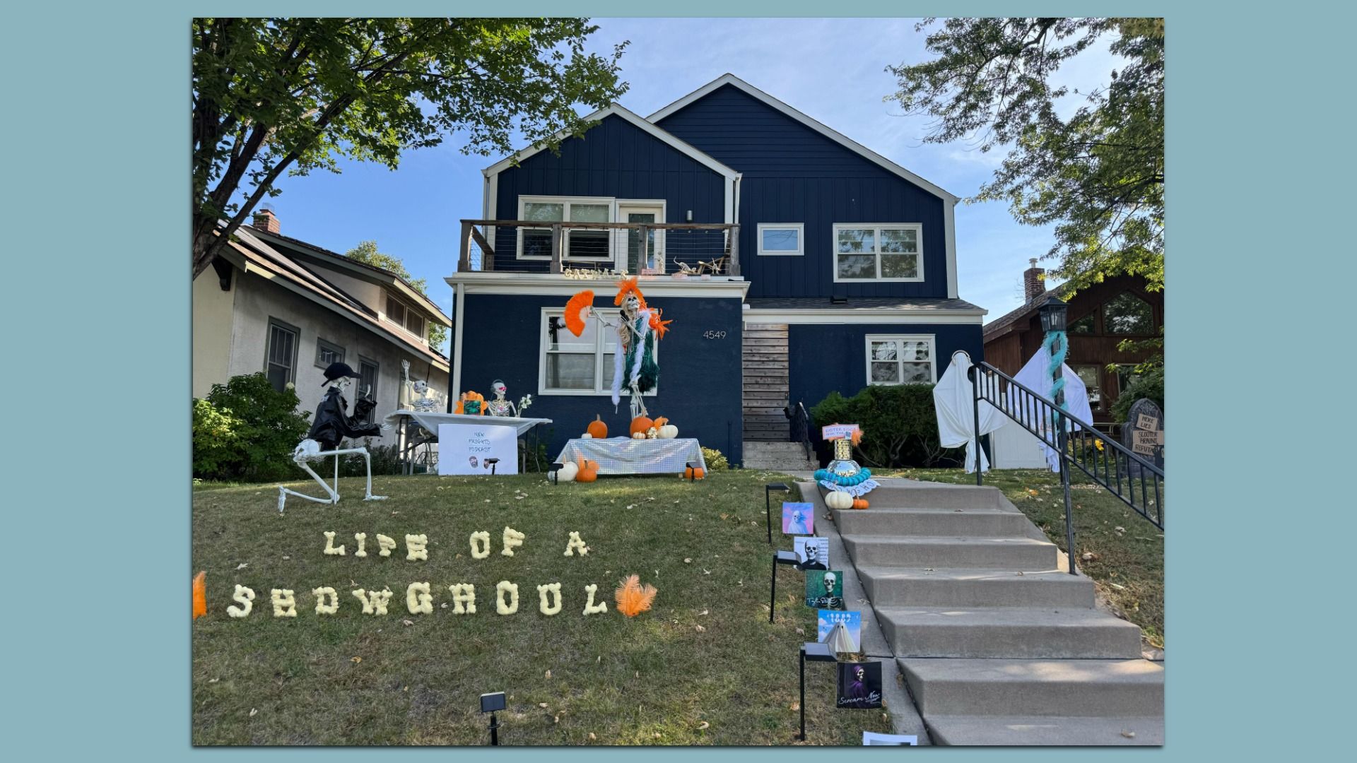 Front yard Halloween display titled "Life of a Showghoul" with skeletons in costumes, pumpkins, and Halloween decorations in front of a navy blue house with white trim and gray stairs.