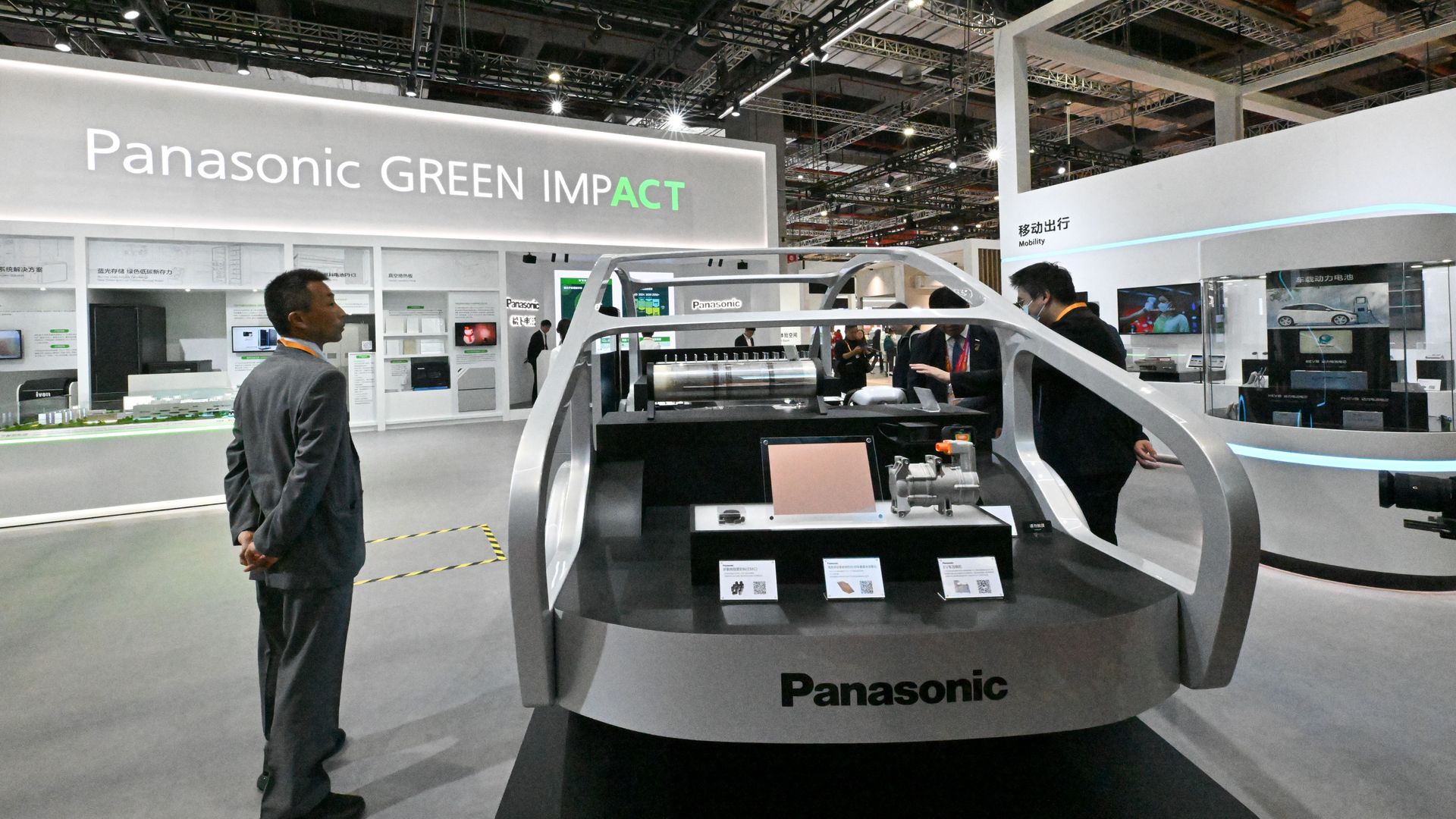 A person in a suit stands next to the shell of a concept car at an auto show booth