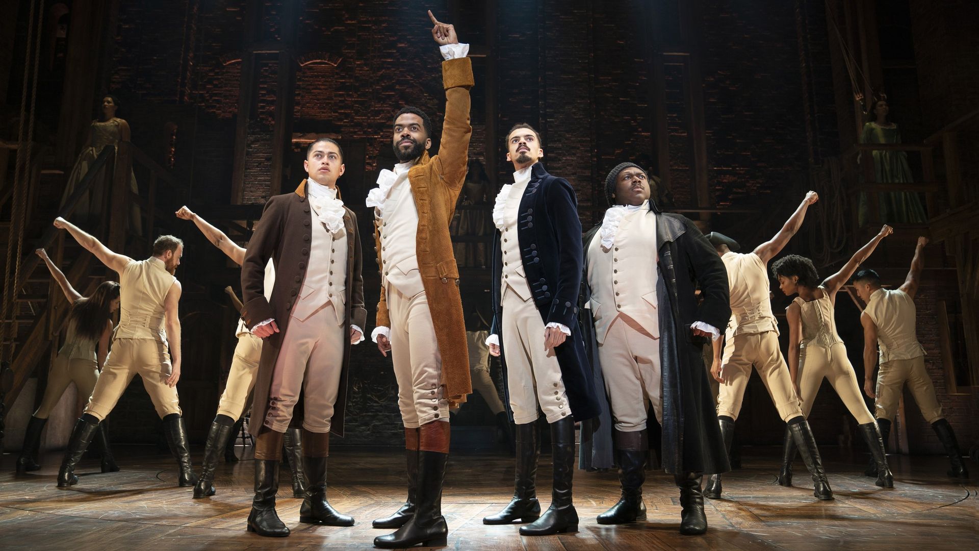 Photo of actors raising their arms on the stage for "Hamilton"