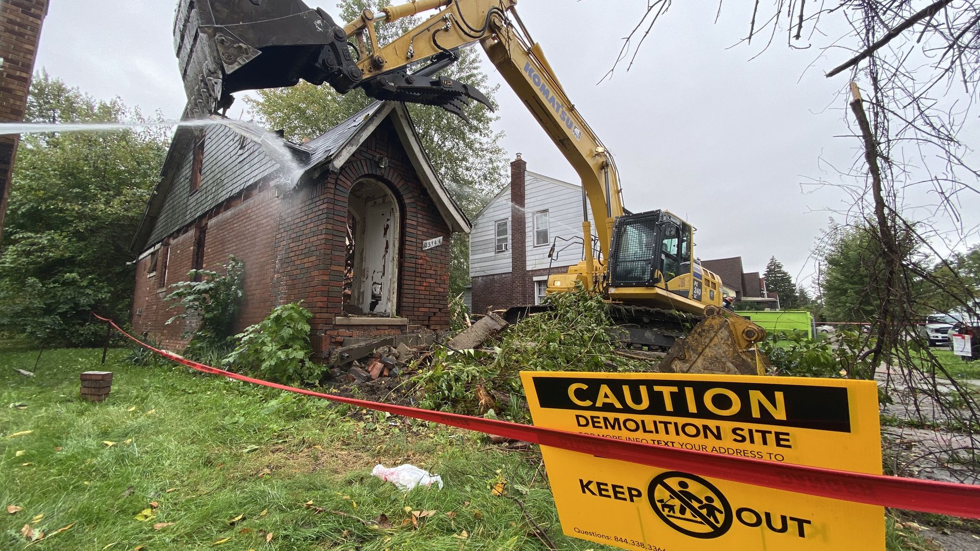 A home getting demolished with a "caution demolition site keep out" sign.