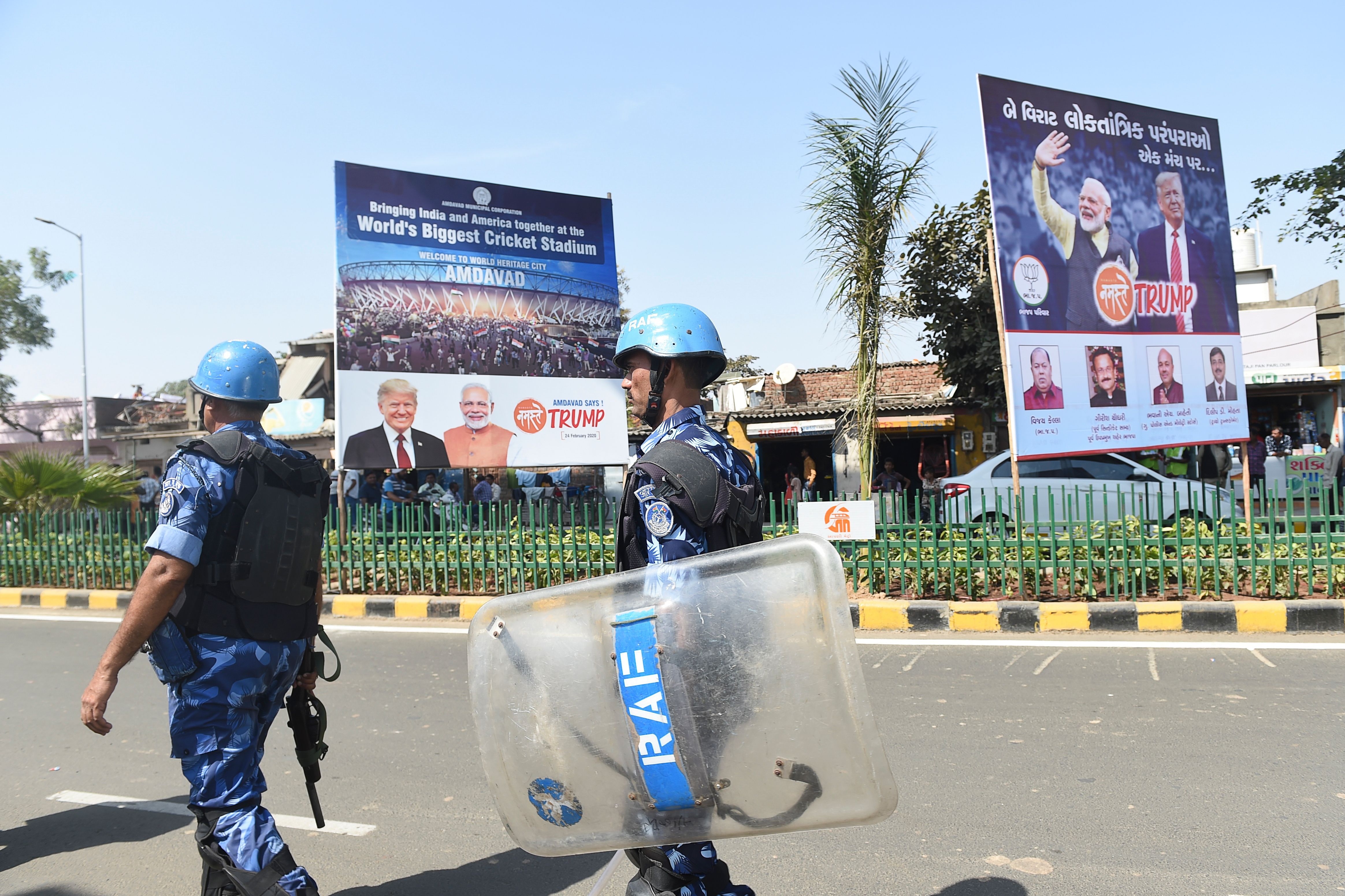 Para-military soldiers from the Rapid Action Force walk past billboards with the images of Trump and Modi, outside the Sardar Patel Stadium, in Motera