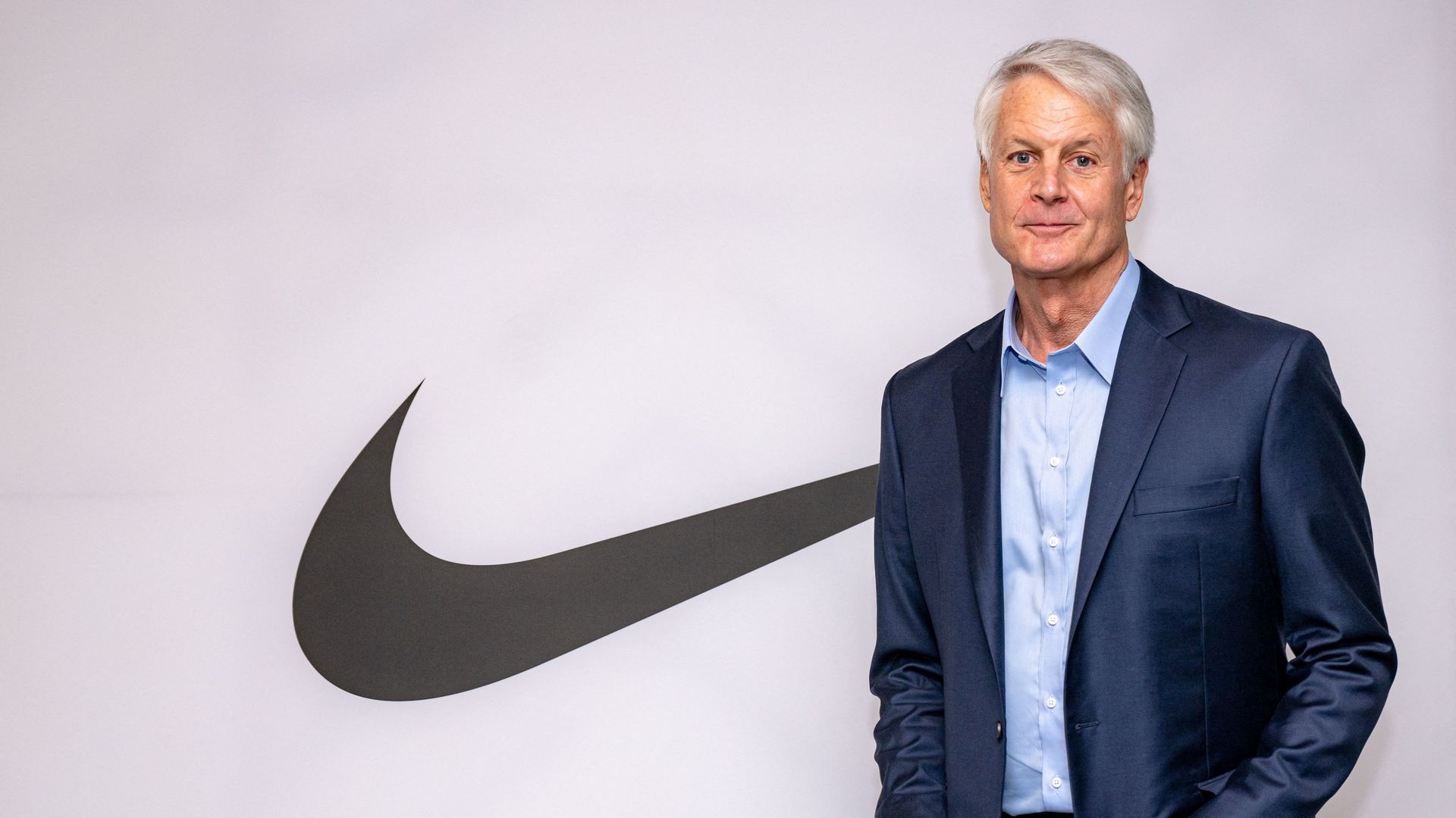   Nike CEO John Donahoe poses for a photo in front of a large, black Nike tick logo against a white background during a visit to Nike European Logistics Campus in Laakdal, June 7, 2023.