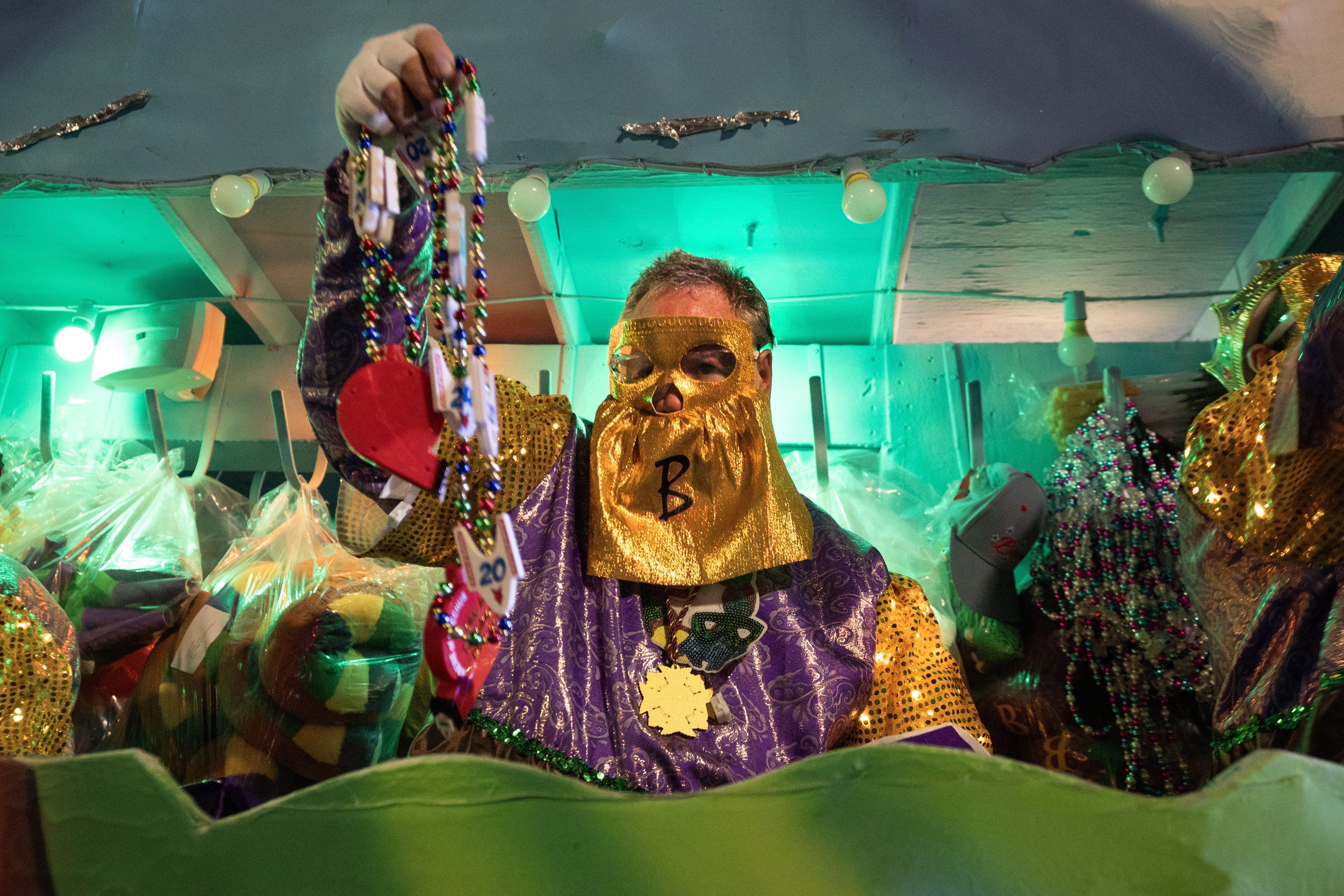 A masked Bacchus krewe-member hands beads toward the camera.