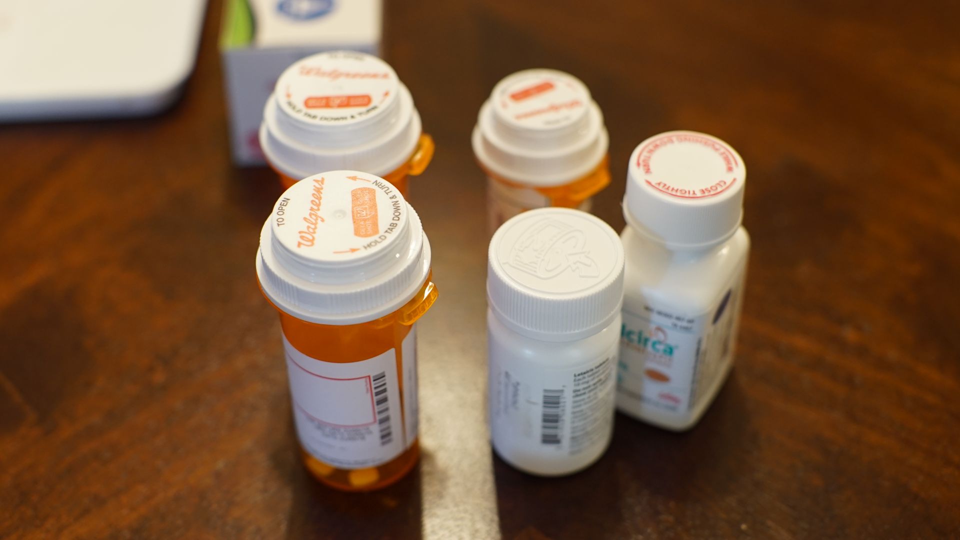 In t his image, six differently shaped orange and white pill bottles sit on a wooden counter. 