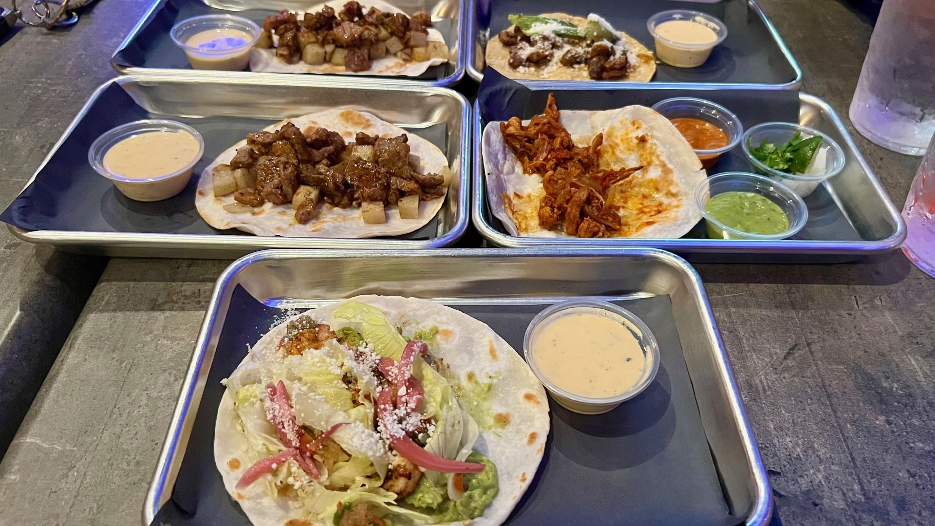 Five trays of one taco each, with sauces on the side