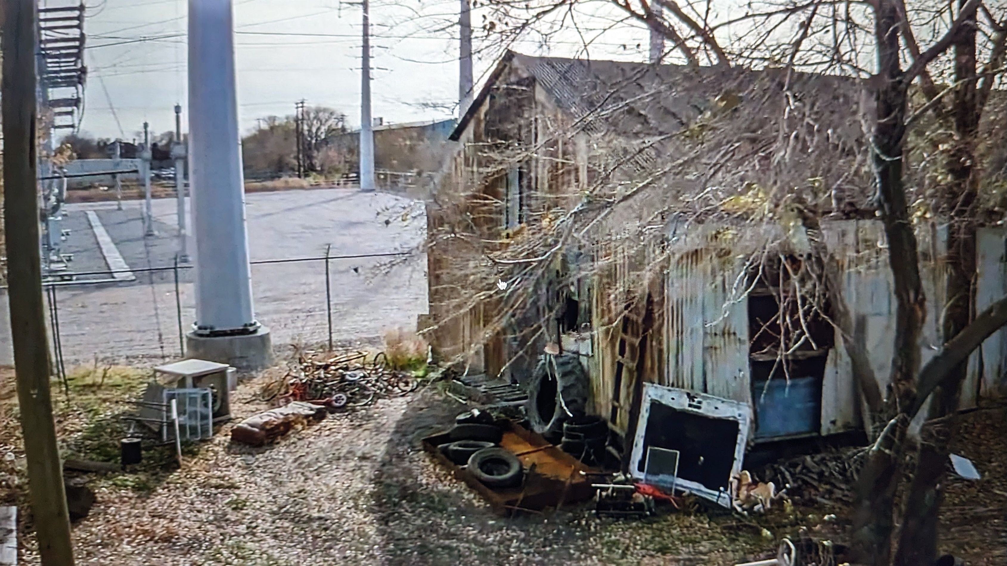 A house of rusty corrugated tin with used belongings on the ground outside of it, next to a power substation.