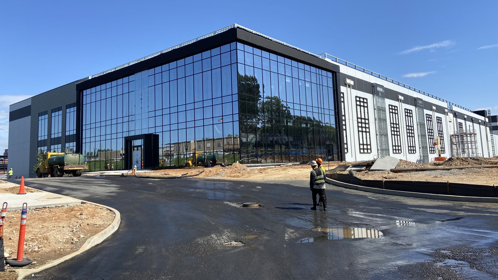 Two construction workers stand in front of a mammoth data center with a front facade of glass