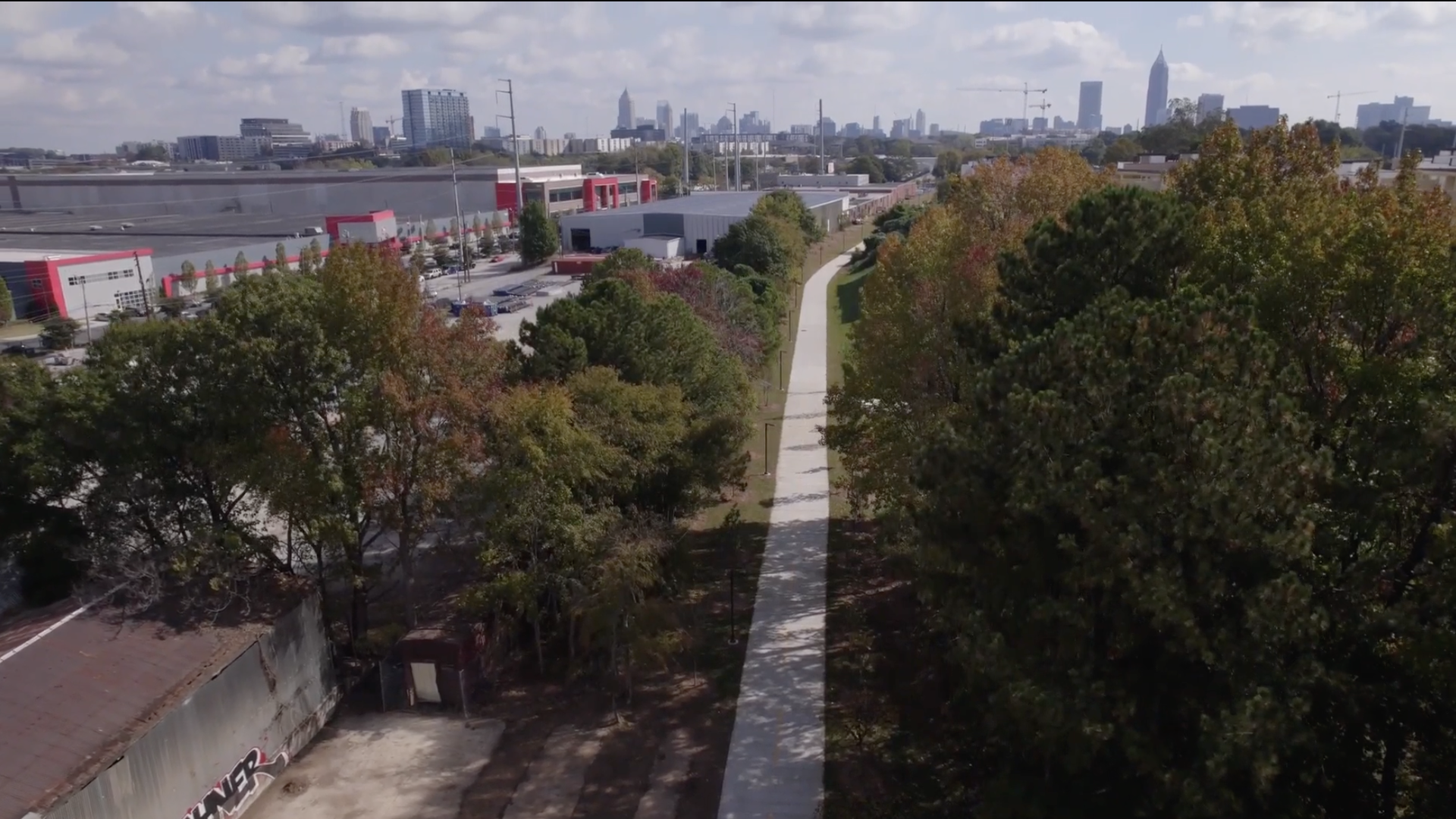 An aerial view of a Beltline path running through trees toward the city skyline of downtown Atlanta