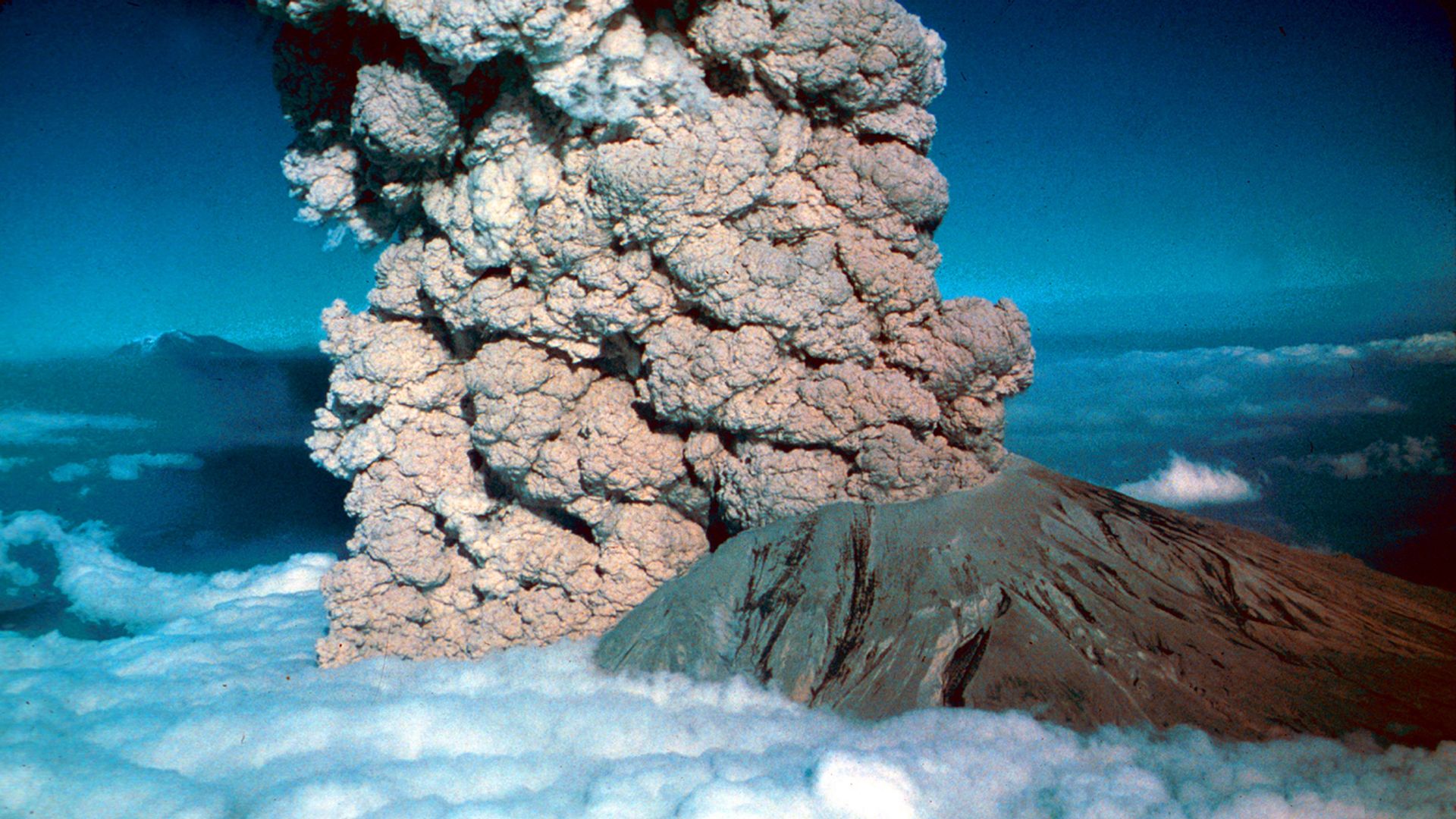 Gray ash is seen against white clouds and blue sky as Mount St. Helens erupts on May 18, 1980. 