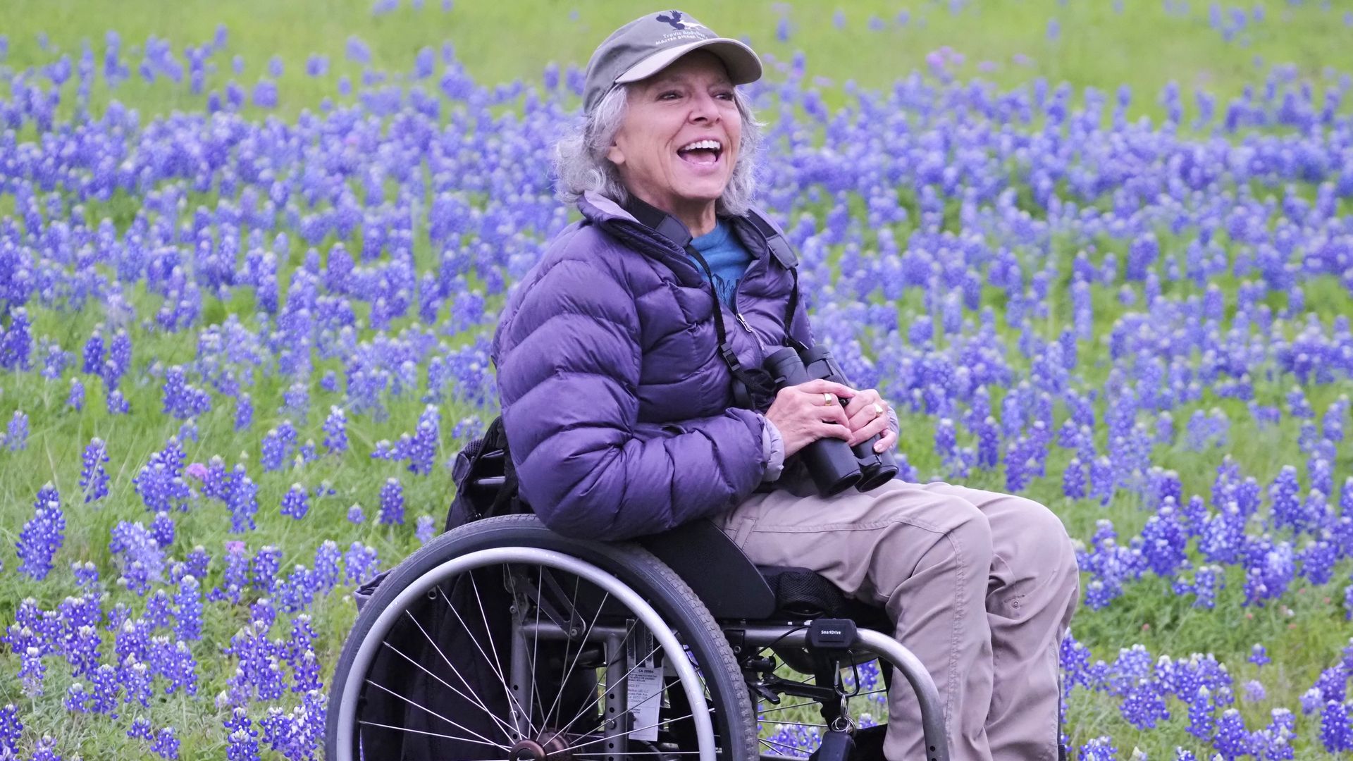 A photo of Virginia Rose in a field of bluebonnets holding her binoculars.