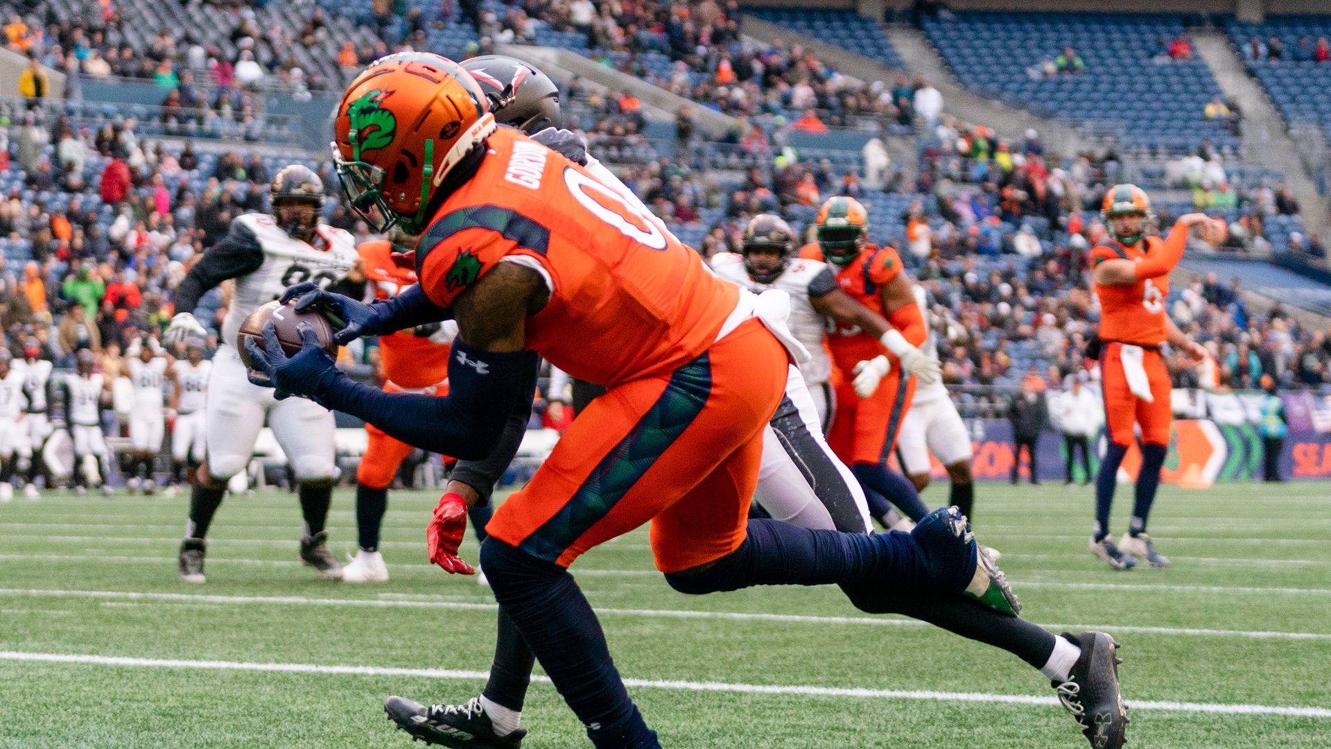 A player in orange and red tries to get a hold of a football with a player in white and blue behind him.