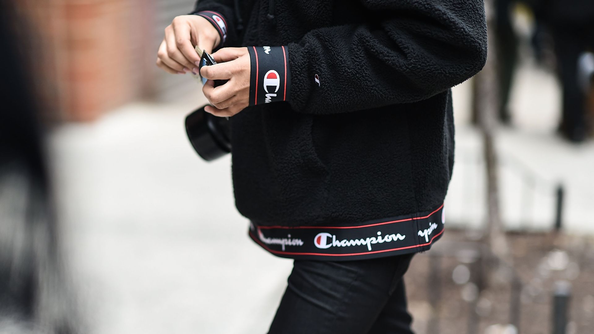 A man walks down a street wearing a black sweatshirt with the Champion logo