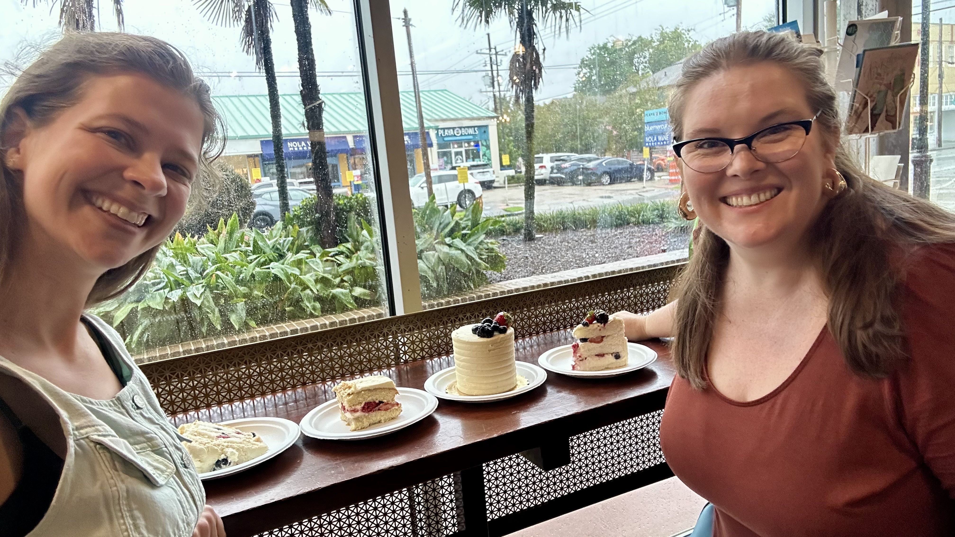 Photo shows Chelsea and Carlie smiling with cakes in Whole Foods.