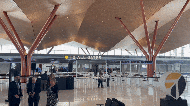 A moving image showing security gates and an atrium under large brown ceilings and orange tree-like columns at the Pittsburgh International Airport.