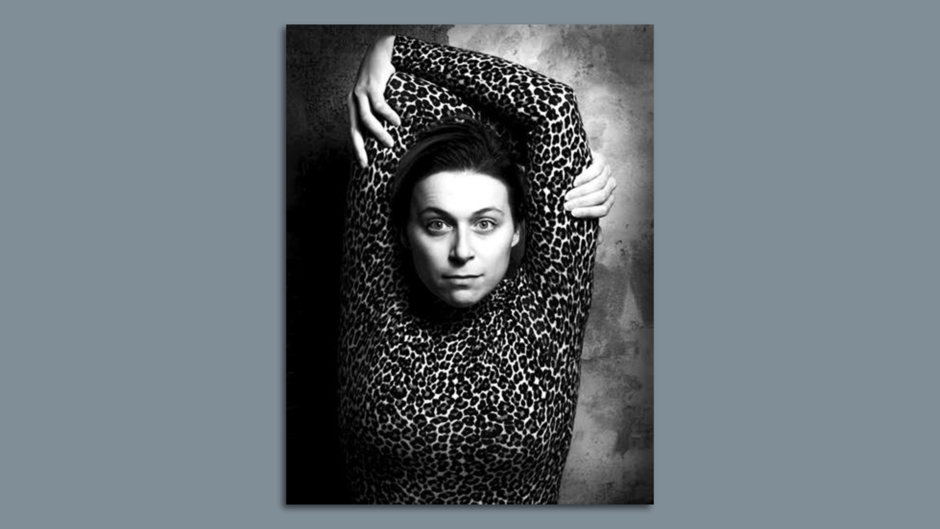 A woman with her arms above her head looks dramatically at the camera.