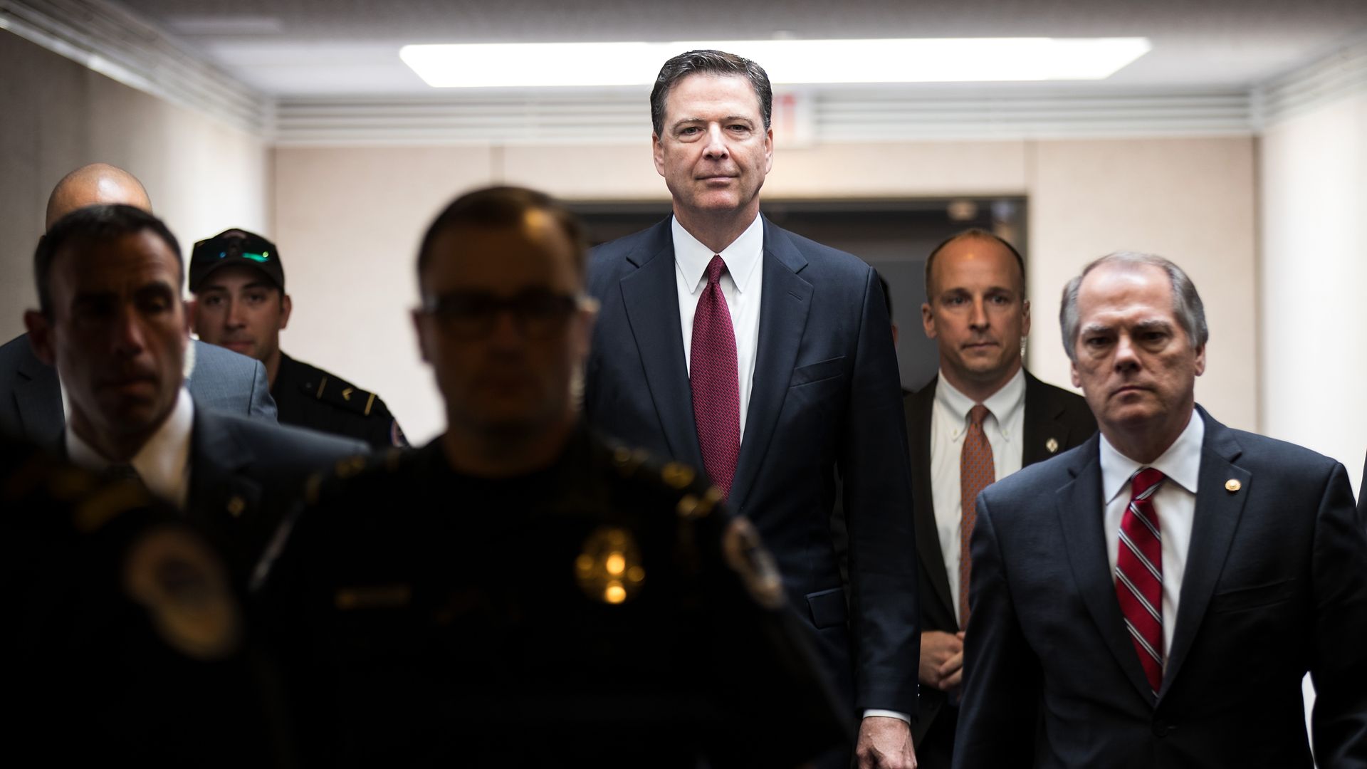 Comey walks down a hallway surrounded by security
