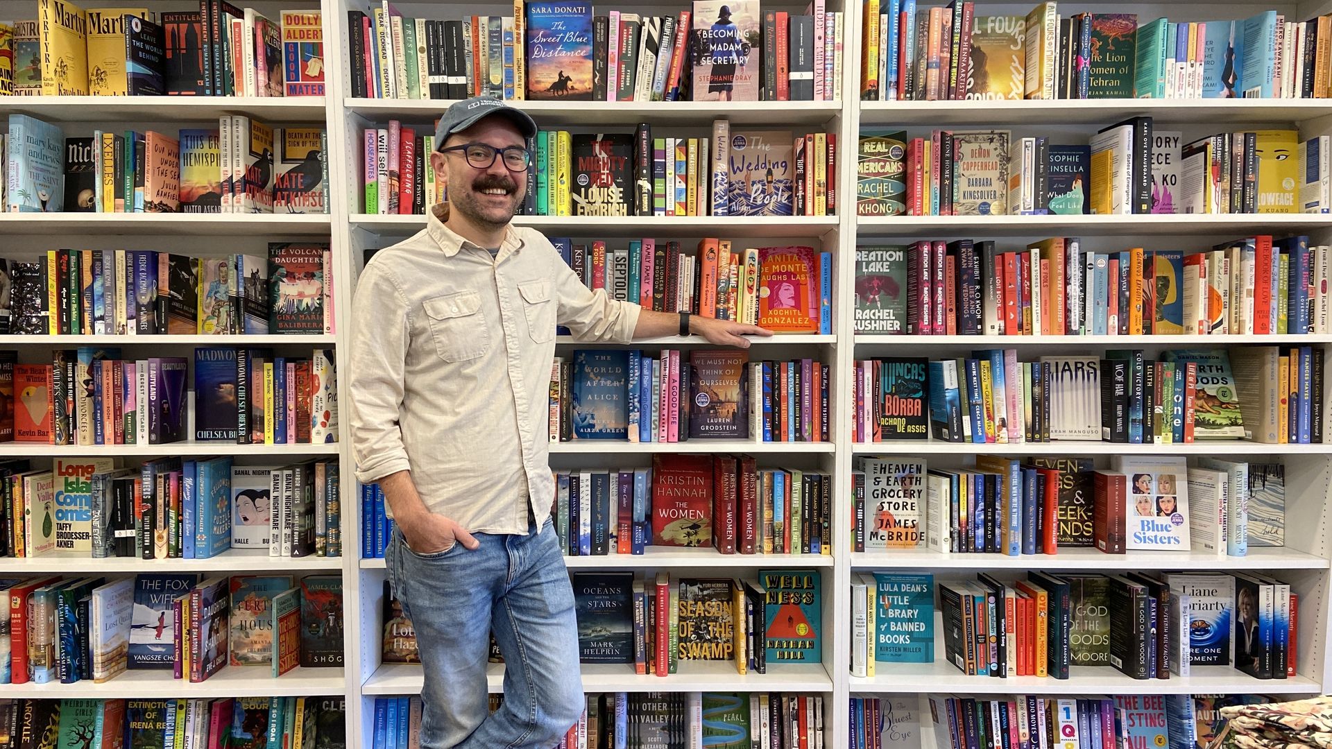 Scott Tynes-Miller standing in front of shelves of books at his shop.
