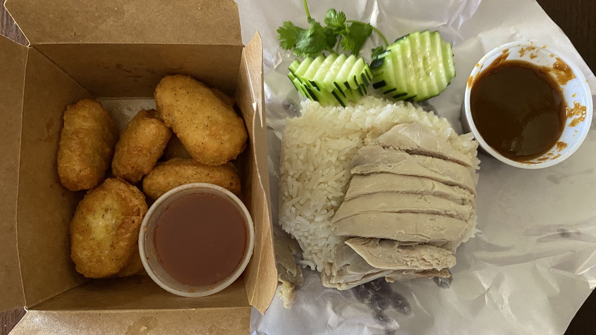 A box of fried chicken nuggets and a plate of sliced chicken over rice