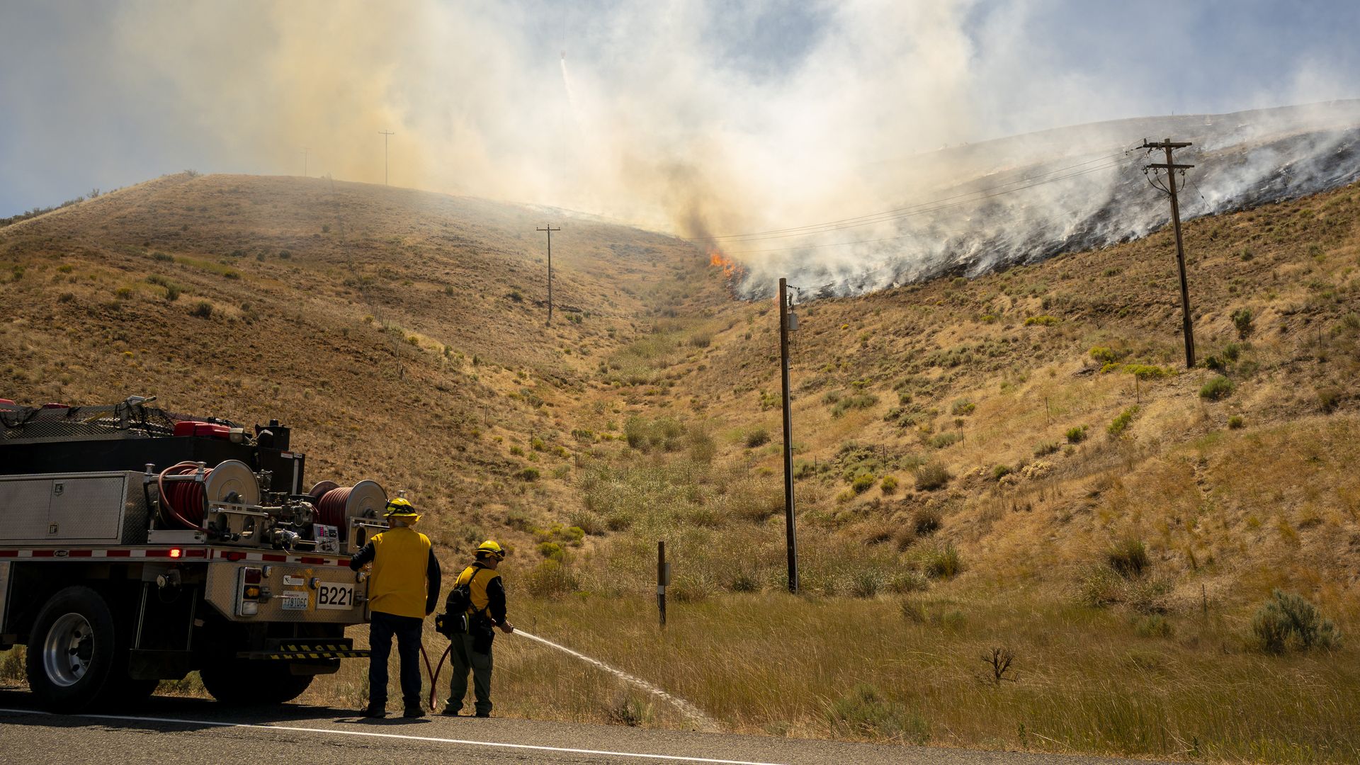 A photo of two firefighters spraying water at the line of the Nessel Road Fire in Washington.