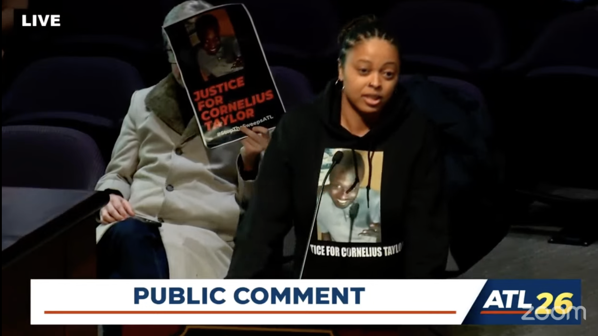 A screenshot of a person wearing a "Justice for Cornelius Taylor" t shirt speaks at a public government meeting