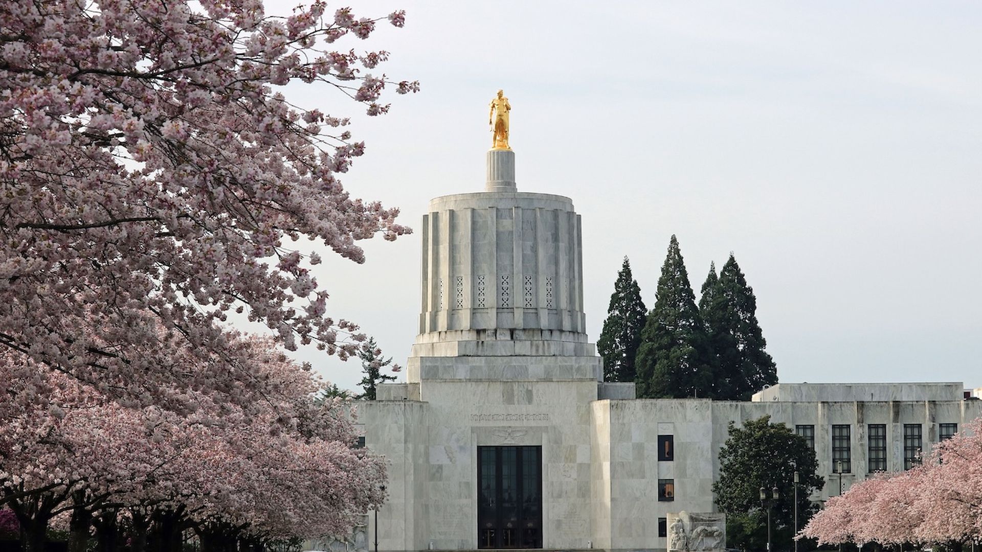 A photo of a white marble building with a round rotunda and a gold figure on the top.