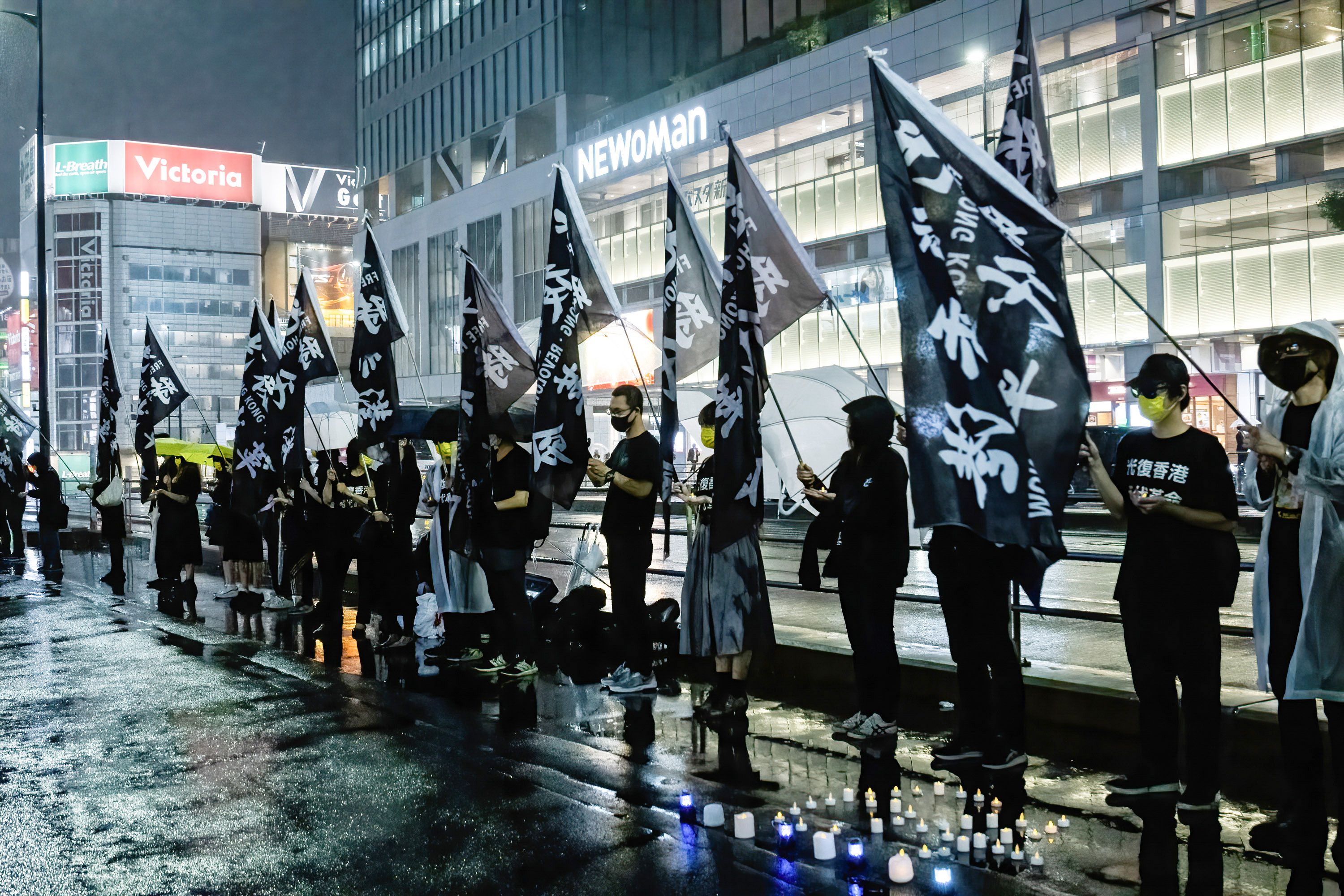 Photo of a line of protesters holding black pro-democracy flags and standing in the rain