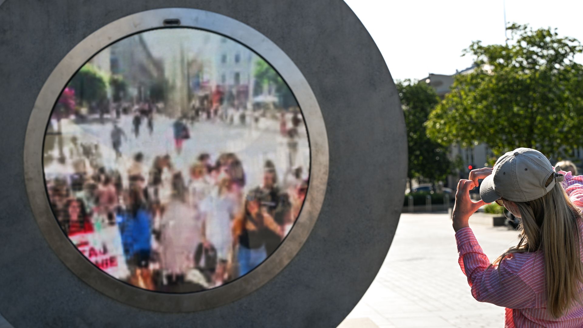 A tourist waves to passersby from Dulin, Ireland, across a virtual bridge, a real-time video portal connecting Lublin with Vilnius and other cities, on July 31, 2024, in Lublin, Lublin Voivodeship, Poland. 