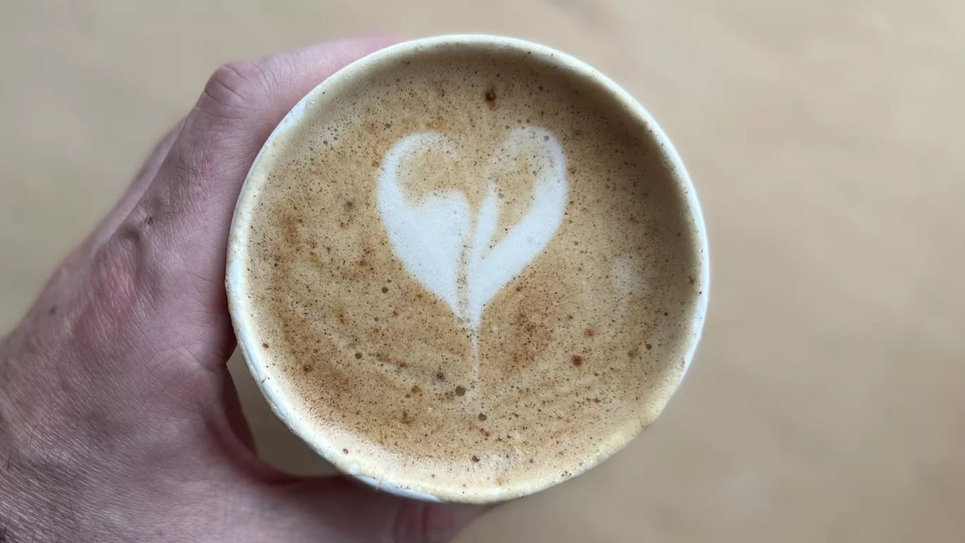 A hand holding a cup of coffee with a heart in the middle of it