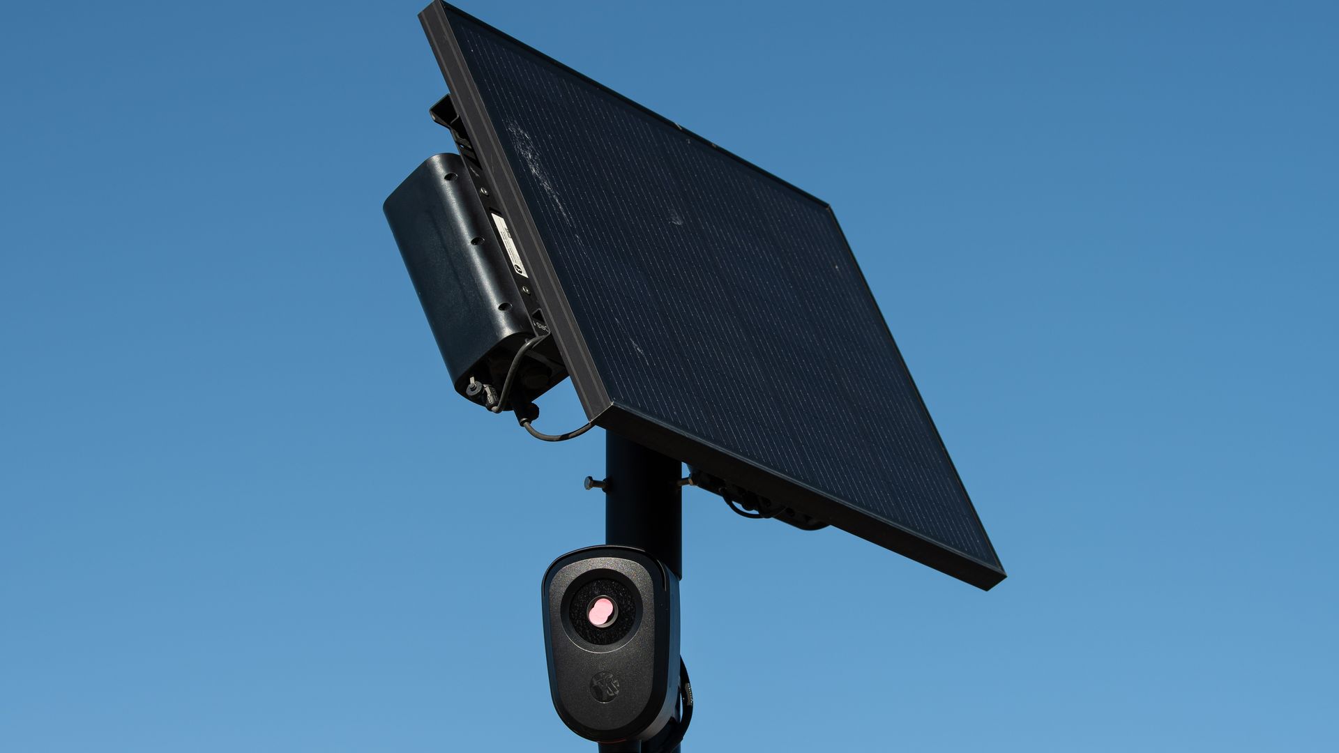 An automated license plate reader is installed on a pole with a bright blue sky in the background.