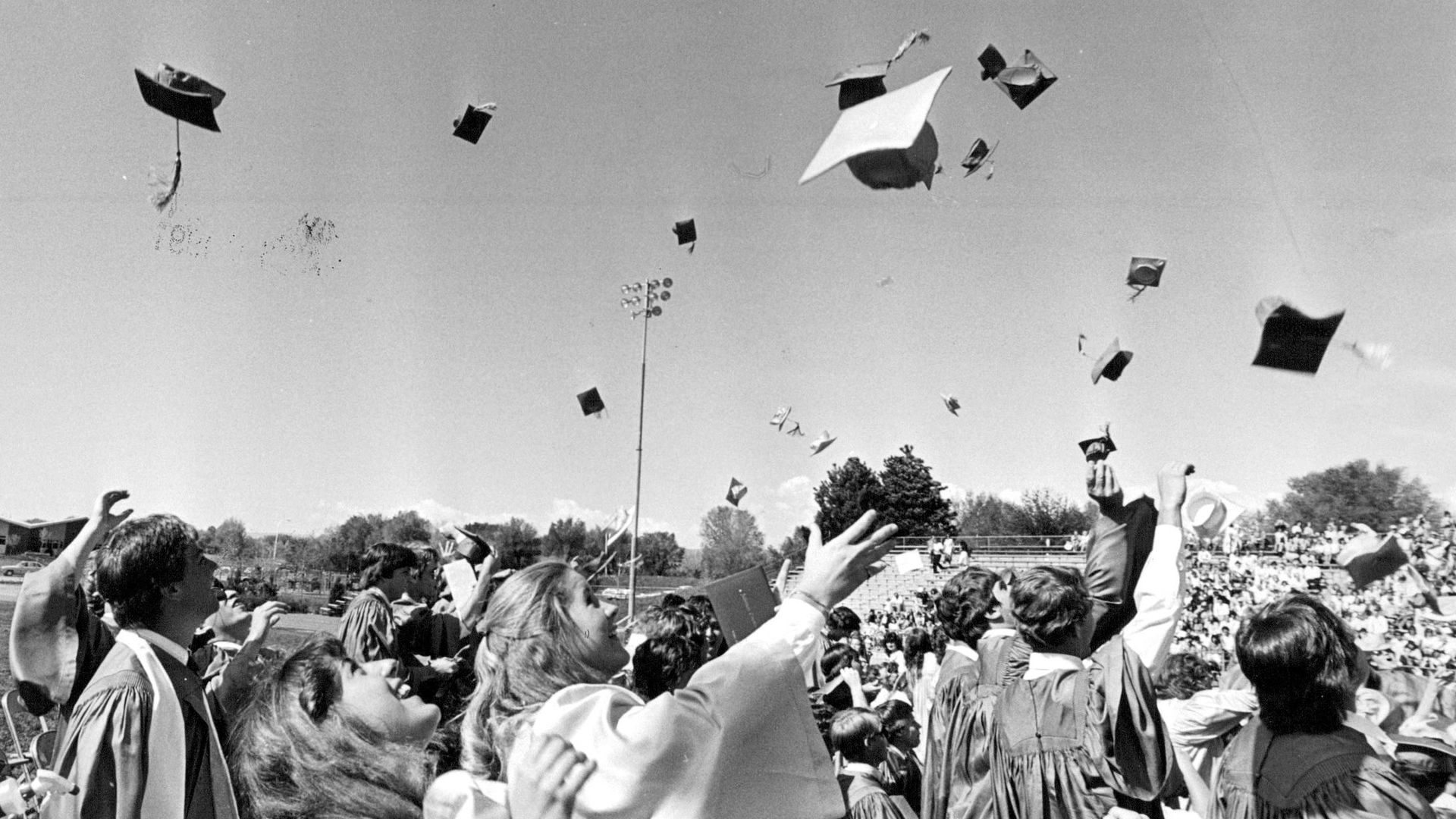Black and white photo of several students in gowns throwing caps into the air