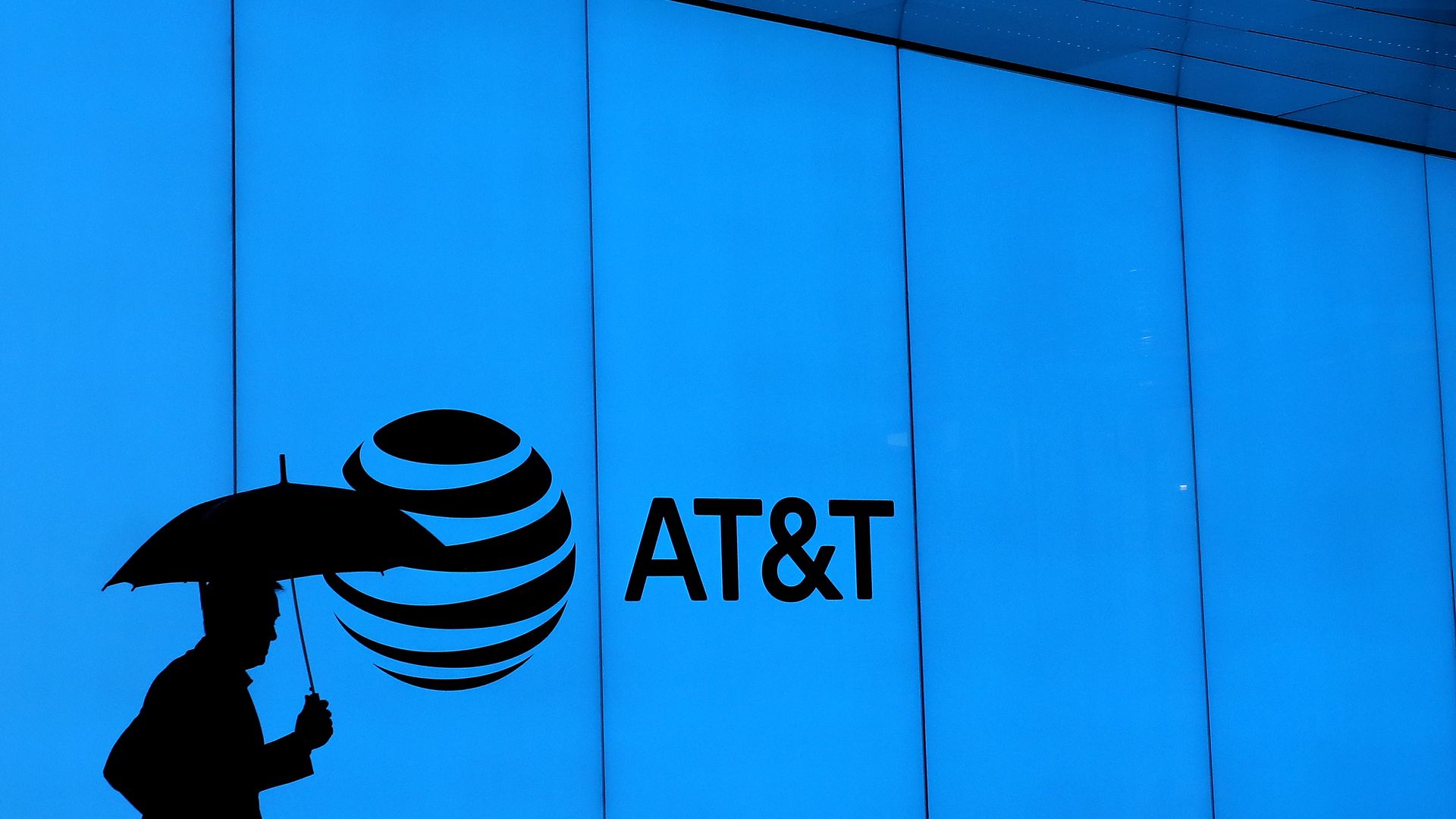 A man walks with an umbrella outside of AT&T corporate headquarters on March 13, 2020 in Dallas, Texas.