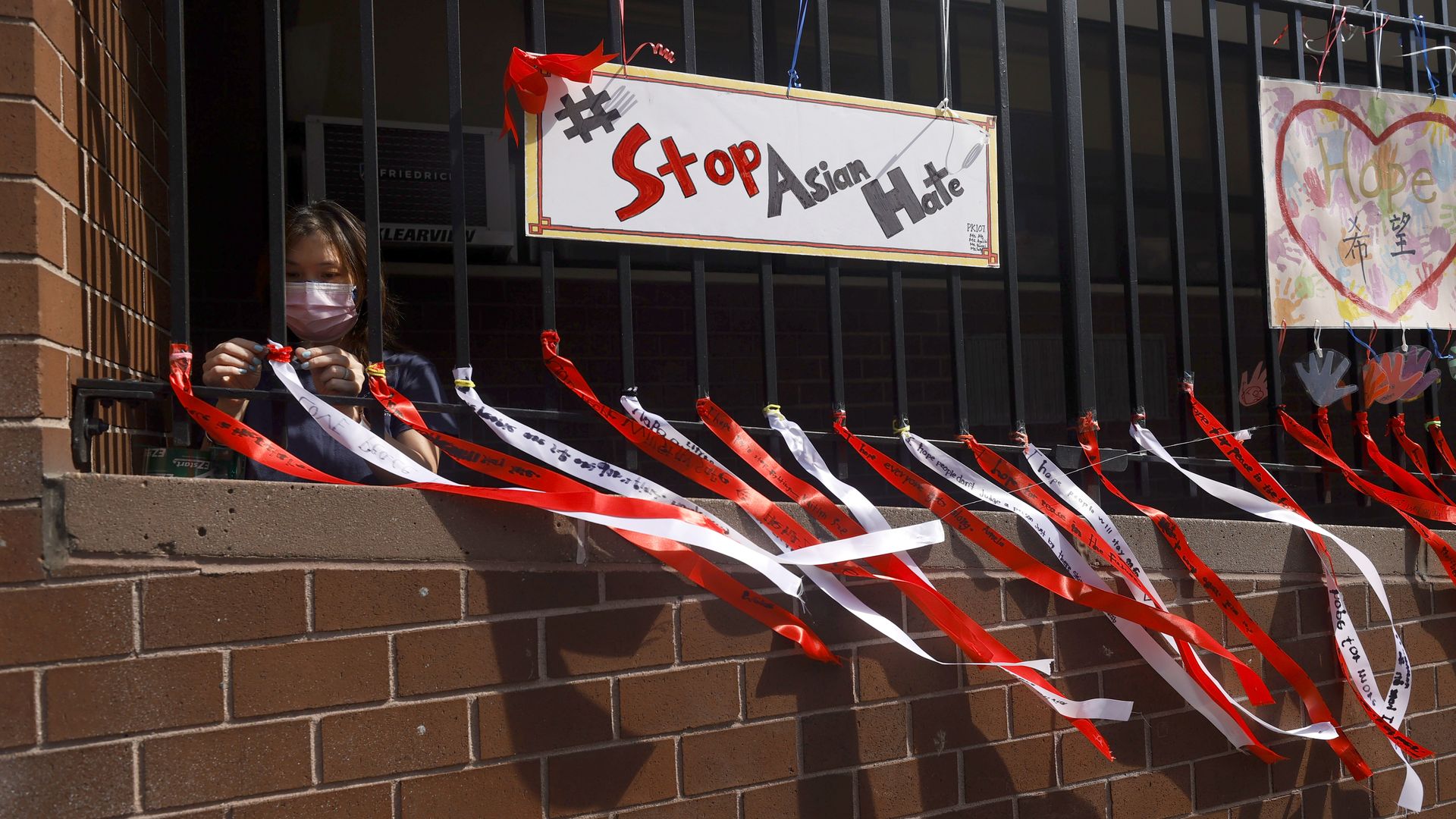 Photo of a person hanging red and white ribbons on a fence with a "Stop Asian Hate" sign