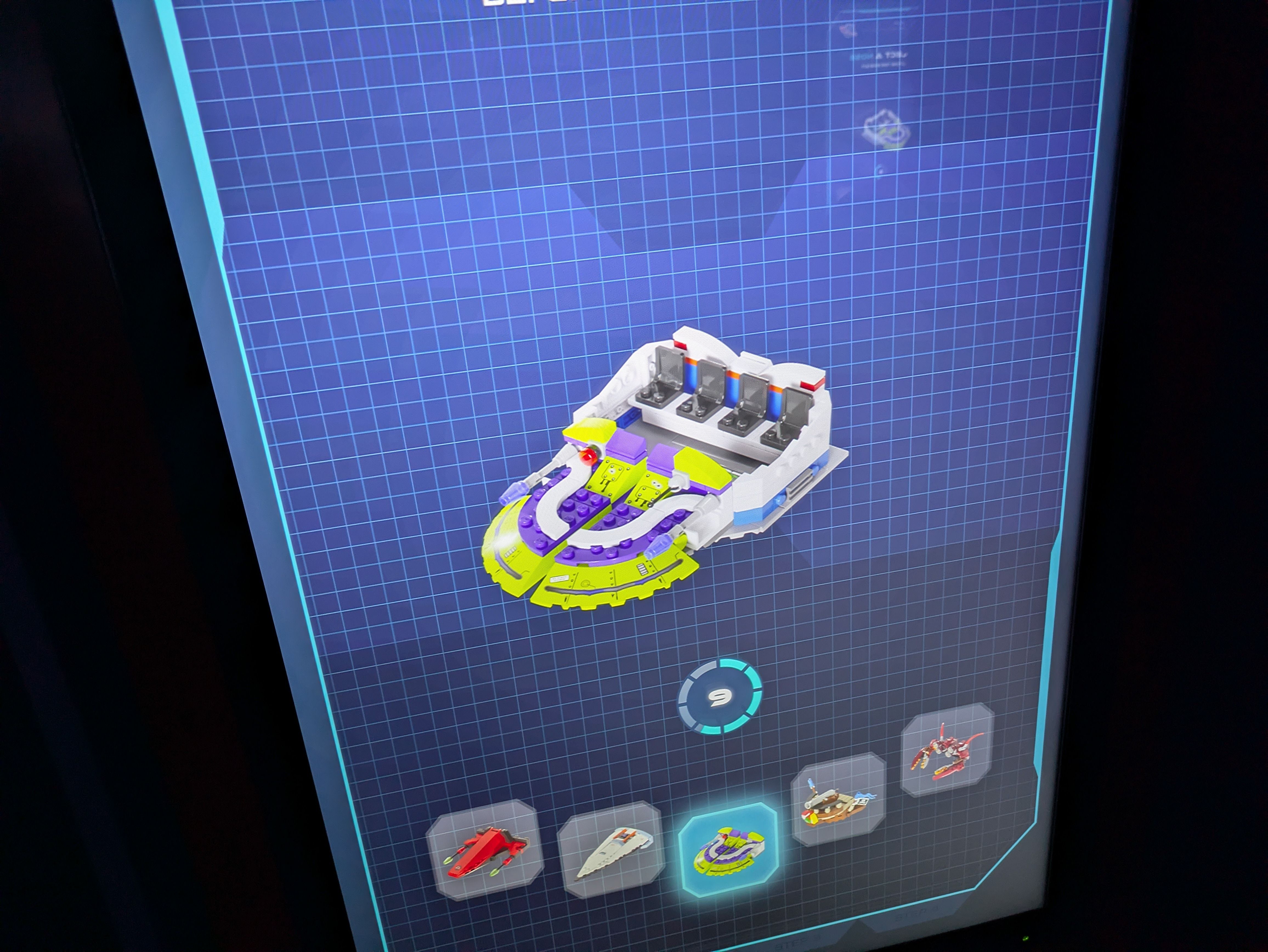 On a blue grid blueprint screen, a colorful LEGO-style hovercraft sits in the center: white hull with purple and yellow accents, exposed seating and cockpit; small model thumbnails along the bottom.